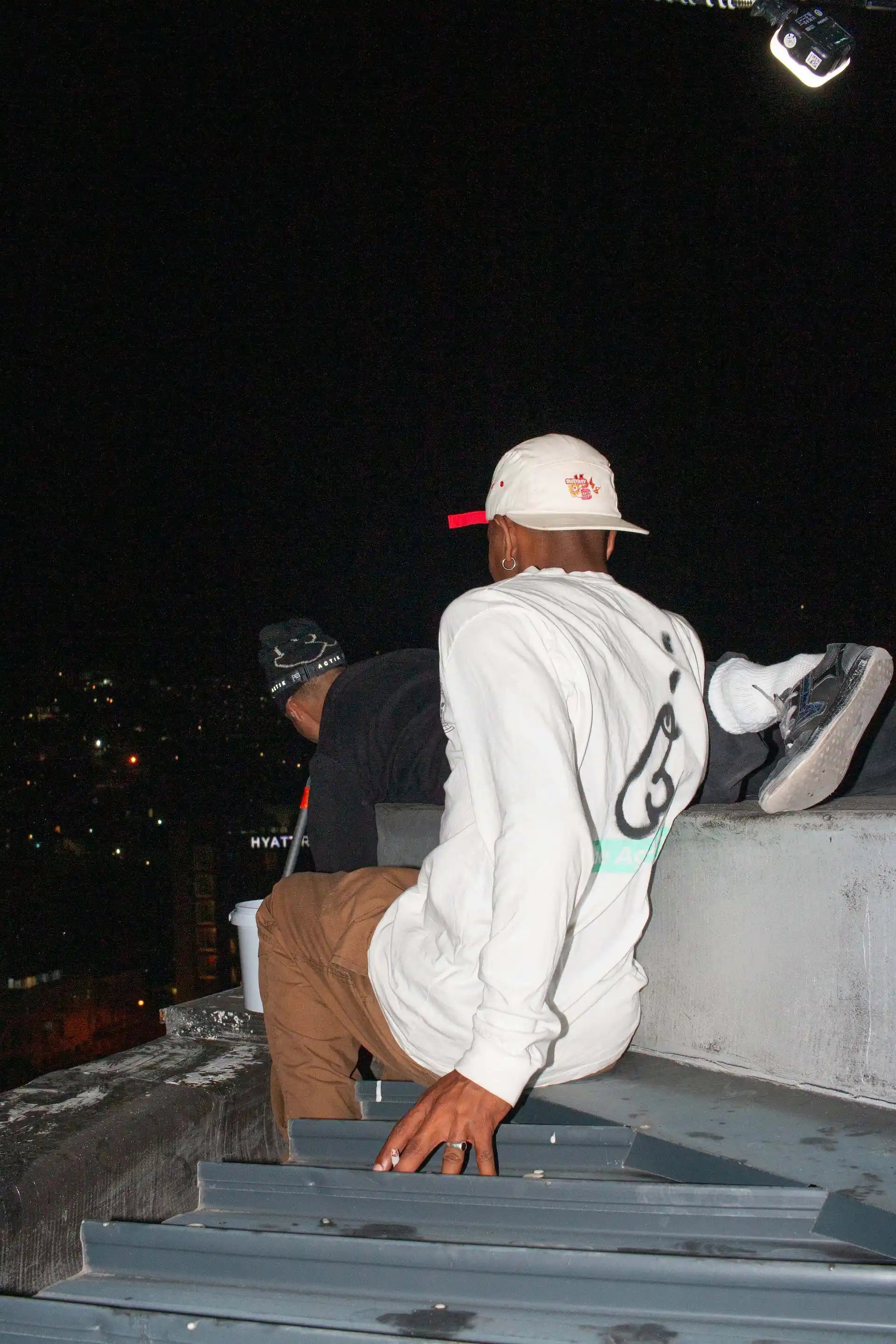 A man in streetwear sits on a rooftop, showcasing South African fashion with a relaxed vibe and urban style
