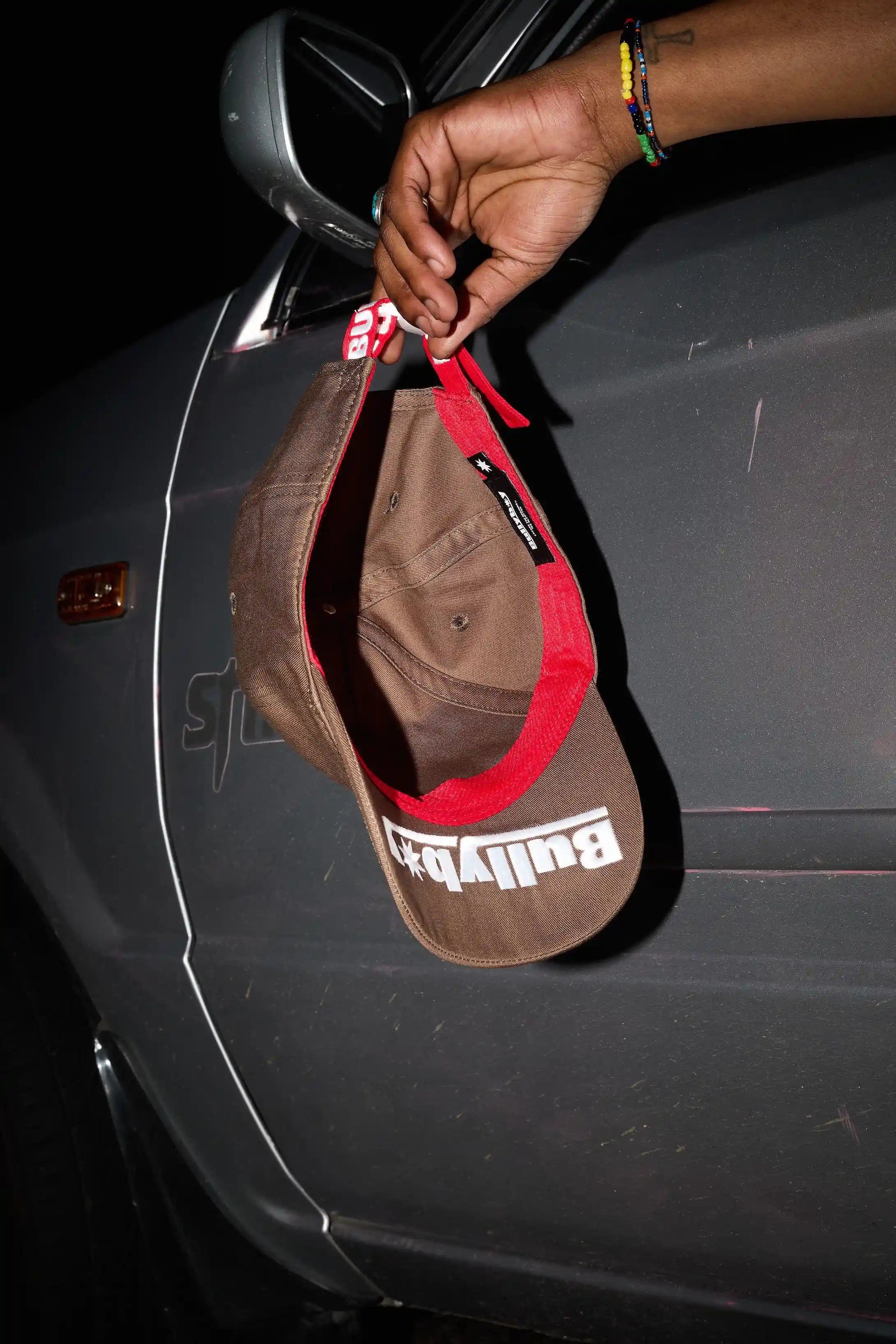 Brown cap with red interior held by a hand against a car door.