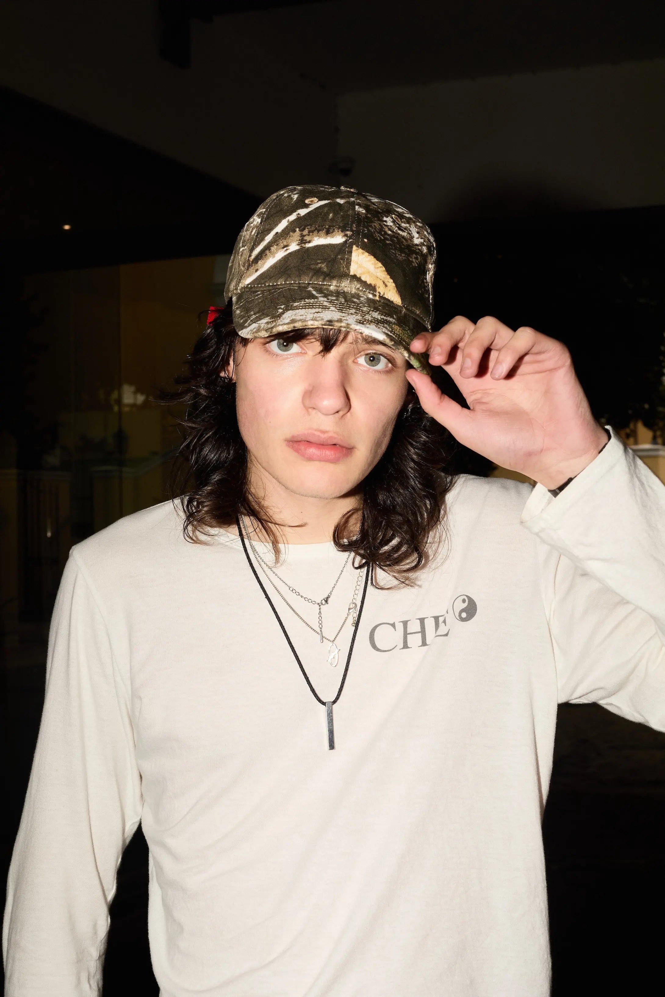 Person wearing a camouflage cap and white long-sleeve shirt with visible branding.