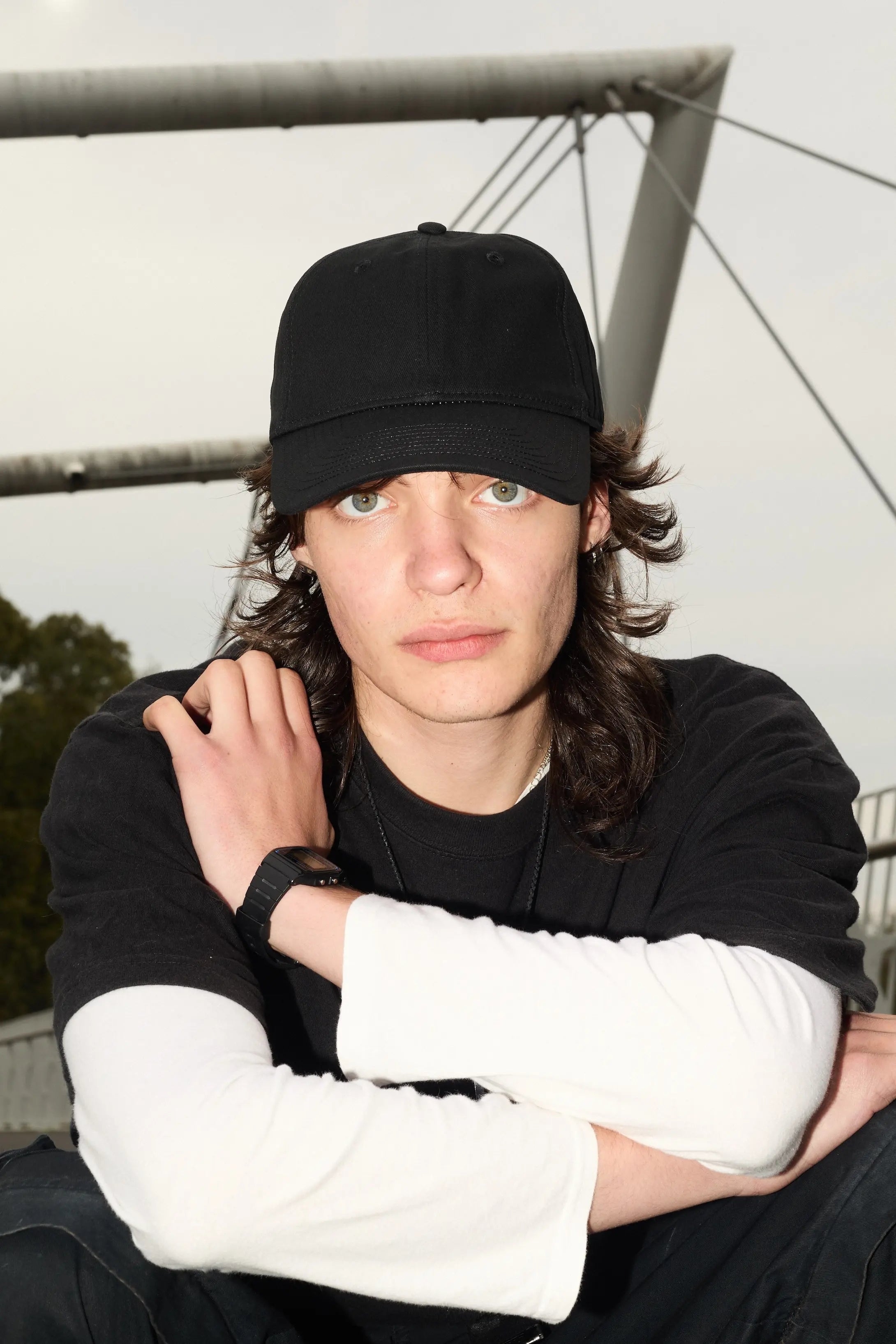 Person wearing a black cap and black shirt with white sleeves, sitting outdoors.