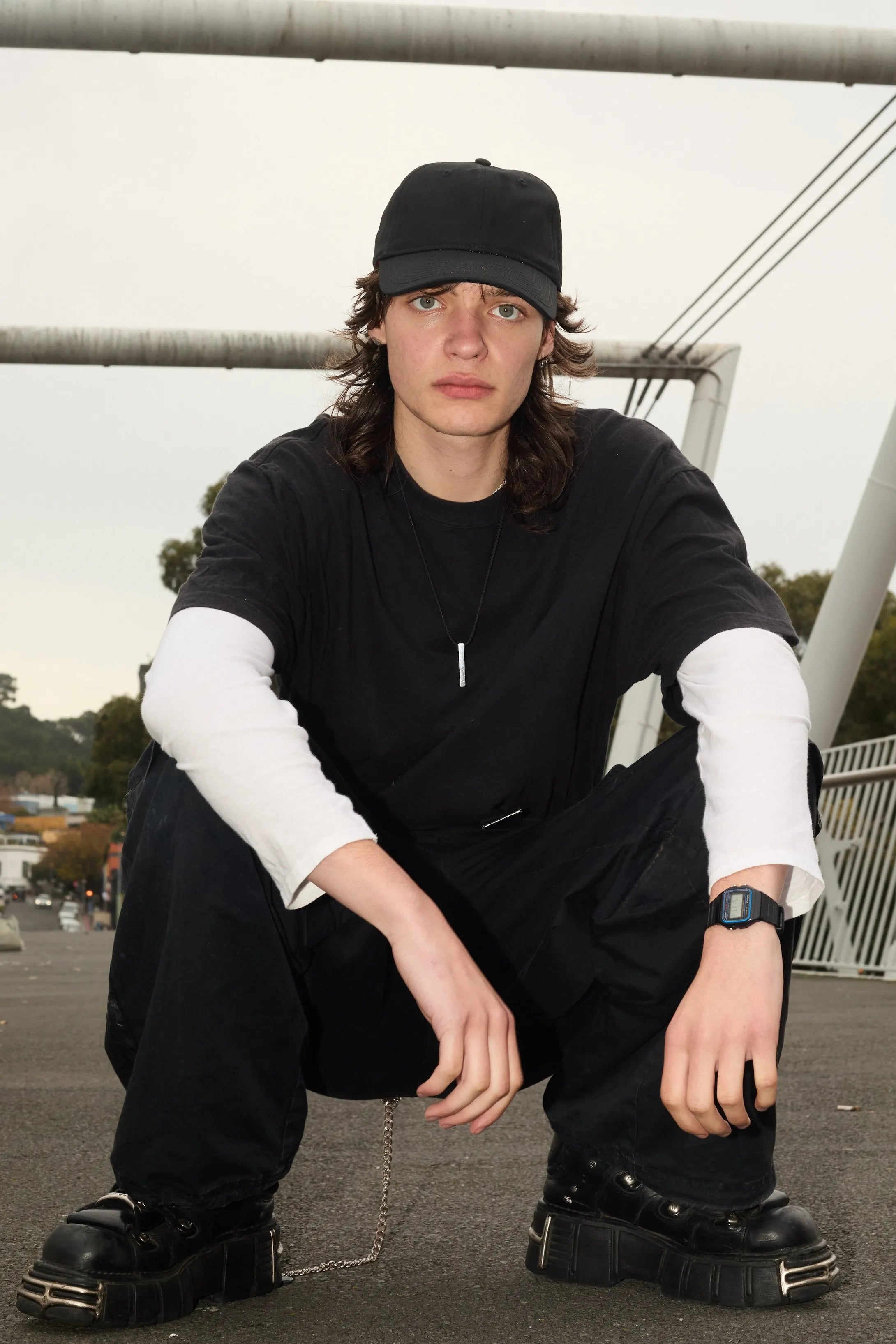 Person wearing a black outfit with a cap, sitting outdoors.