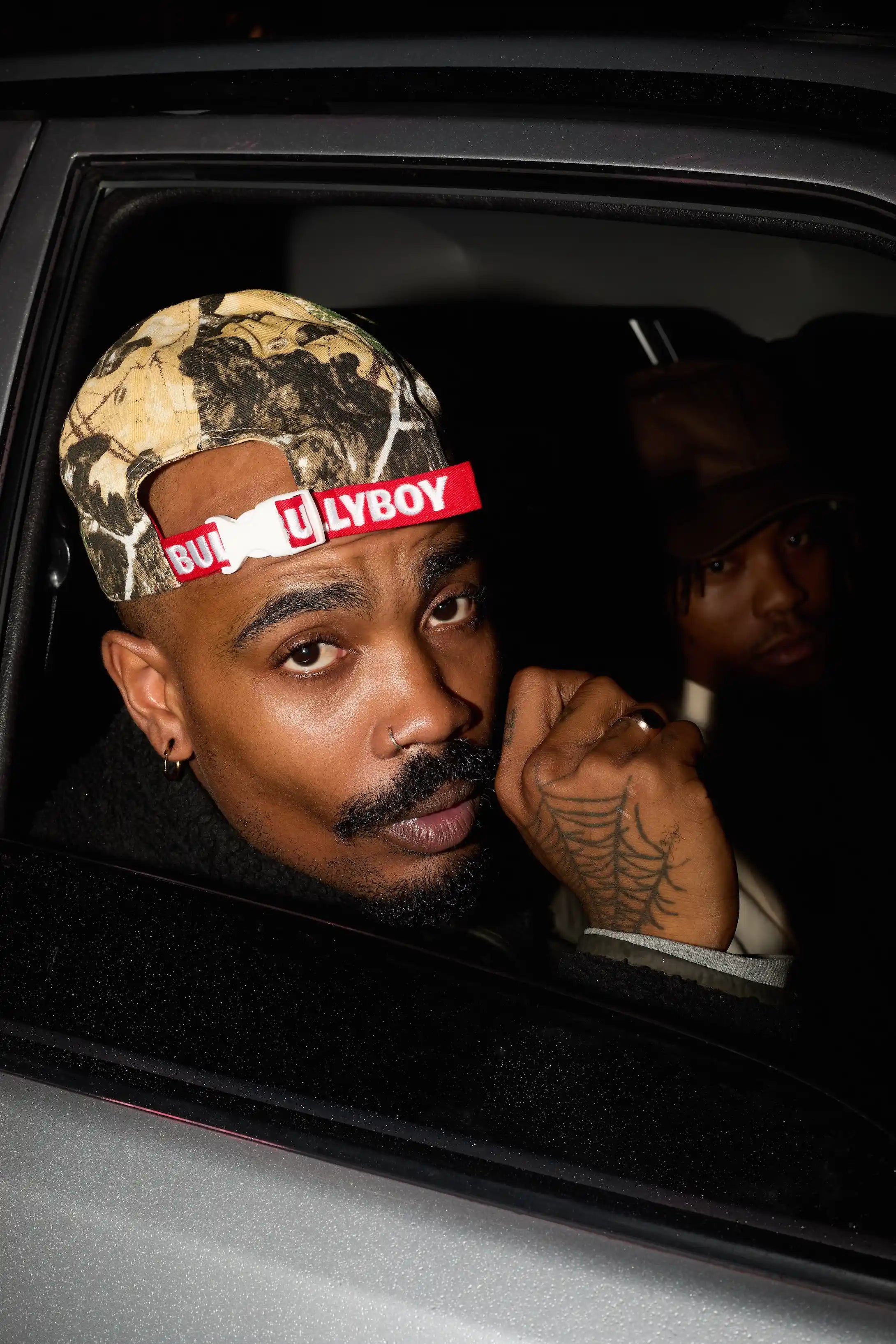 Man wearing a cap with 'Gucci' and 'LYBOY' branding inside a car.
