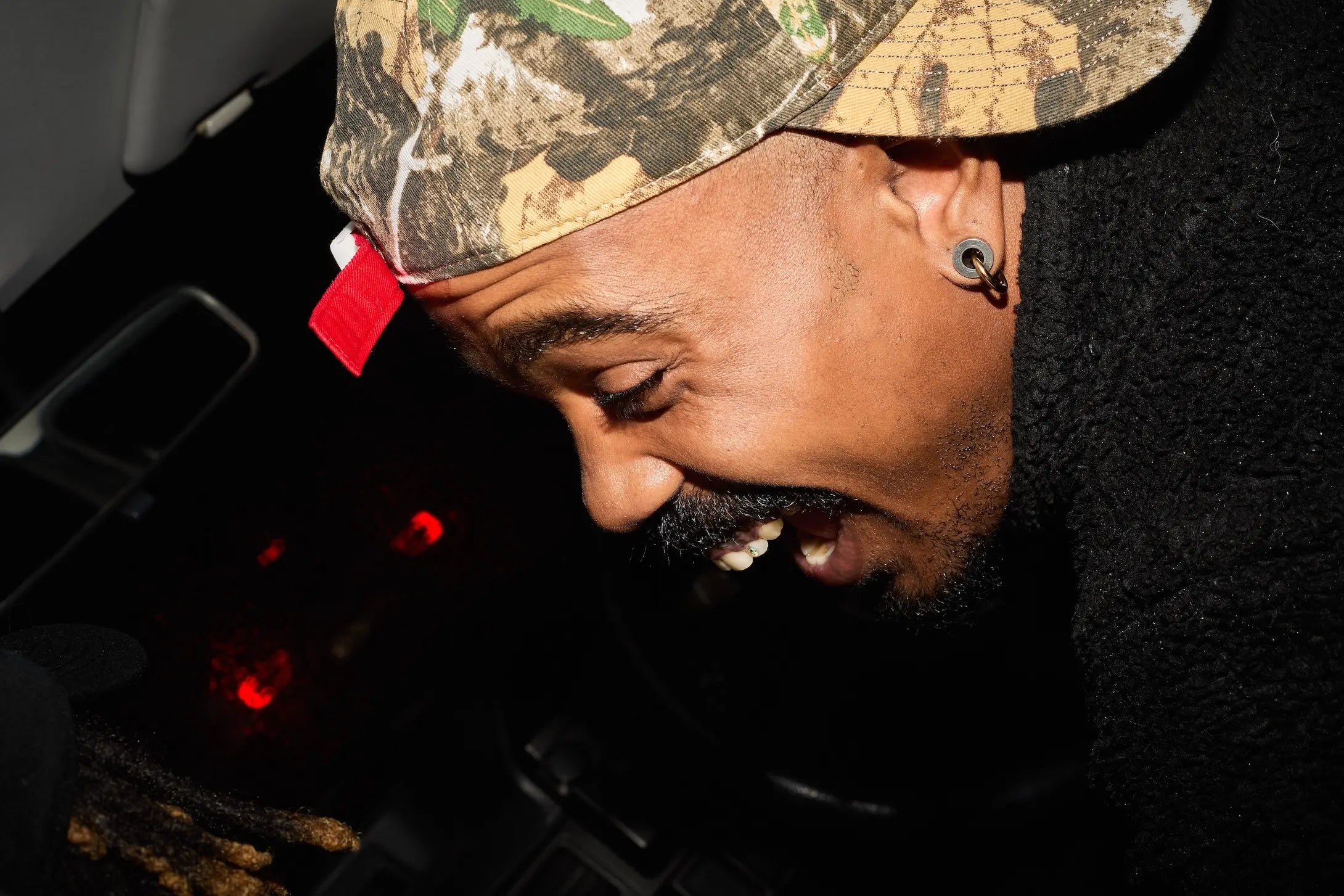 Person wearing a camouflage cap with a red tag inside a vehicle