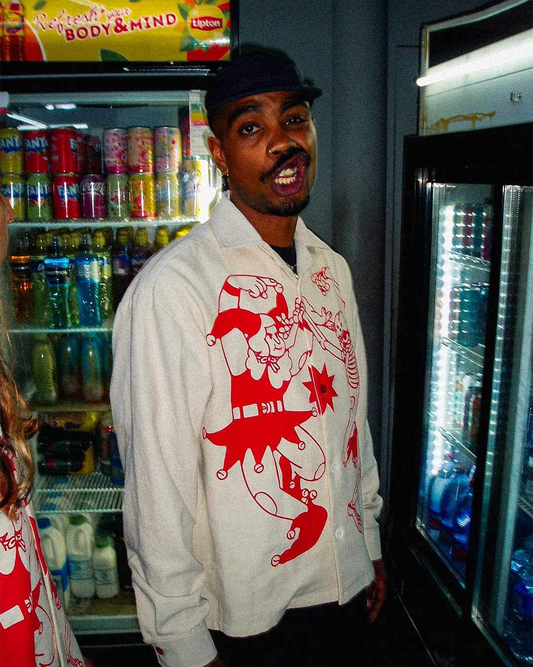 Man wearing a white jacket with red graphics in front of a refrigerator.