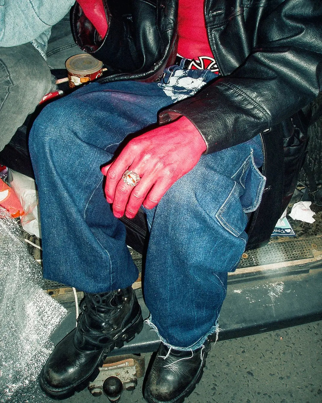 Person wearing blue jeans, black leather jacket, and black boots sitting on a step.