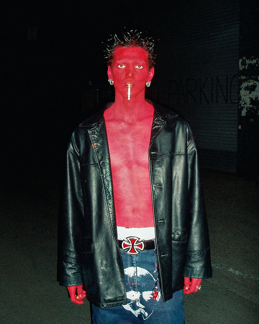 Person wearing a black leather jacket with a red shirt and red gloves in a dark setting.