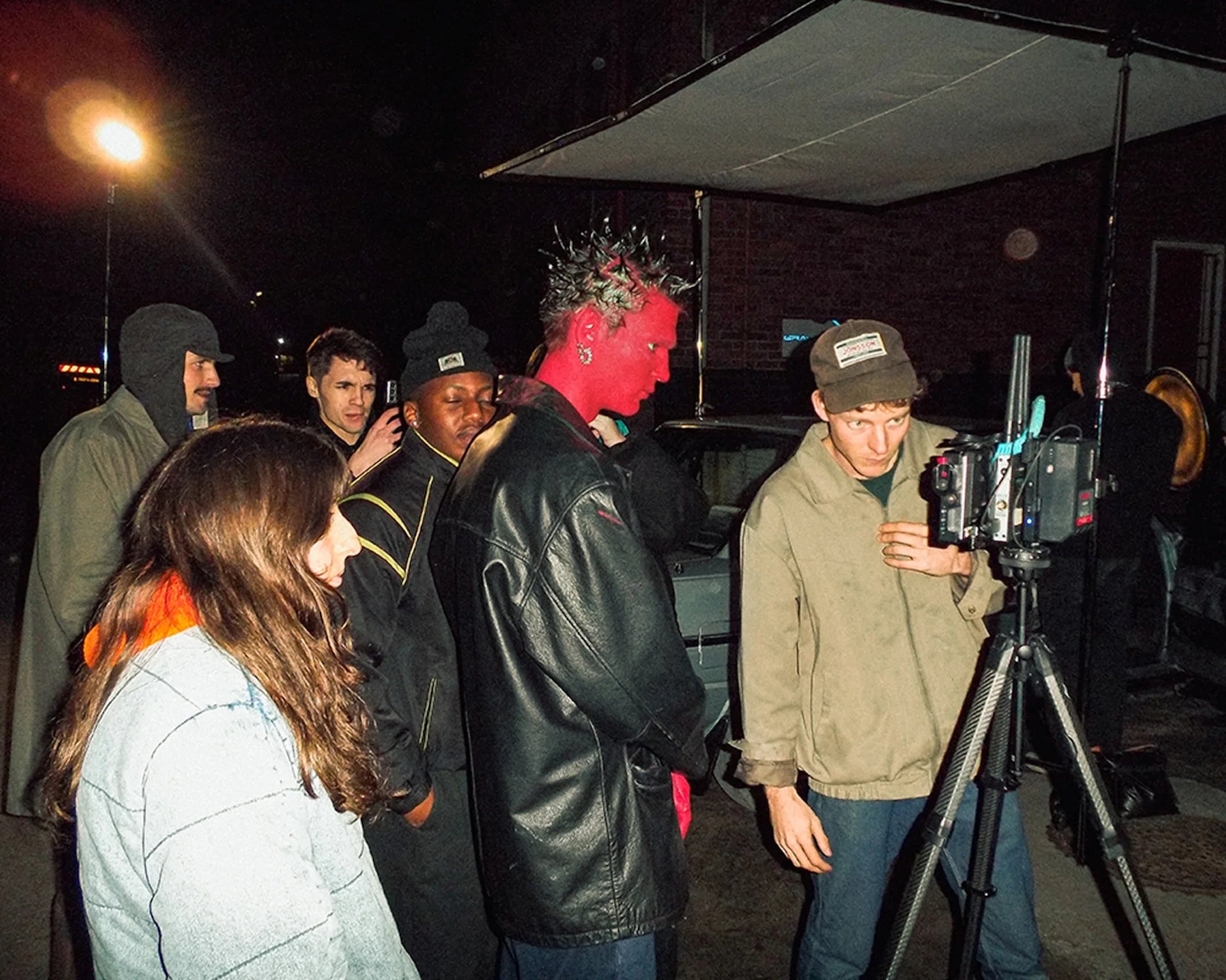Person with red makeup interacting with others on a film set at night.