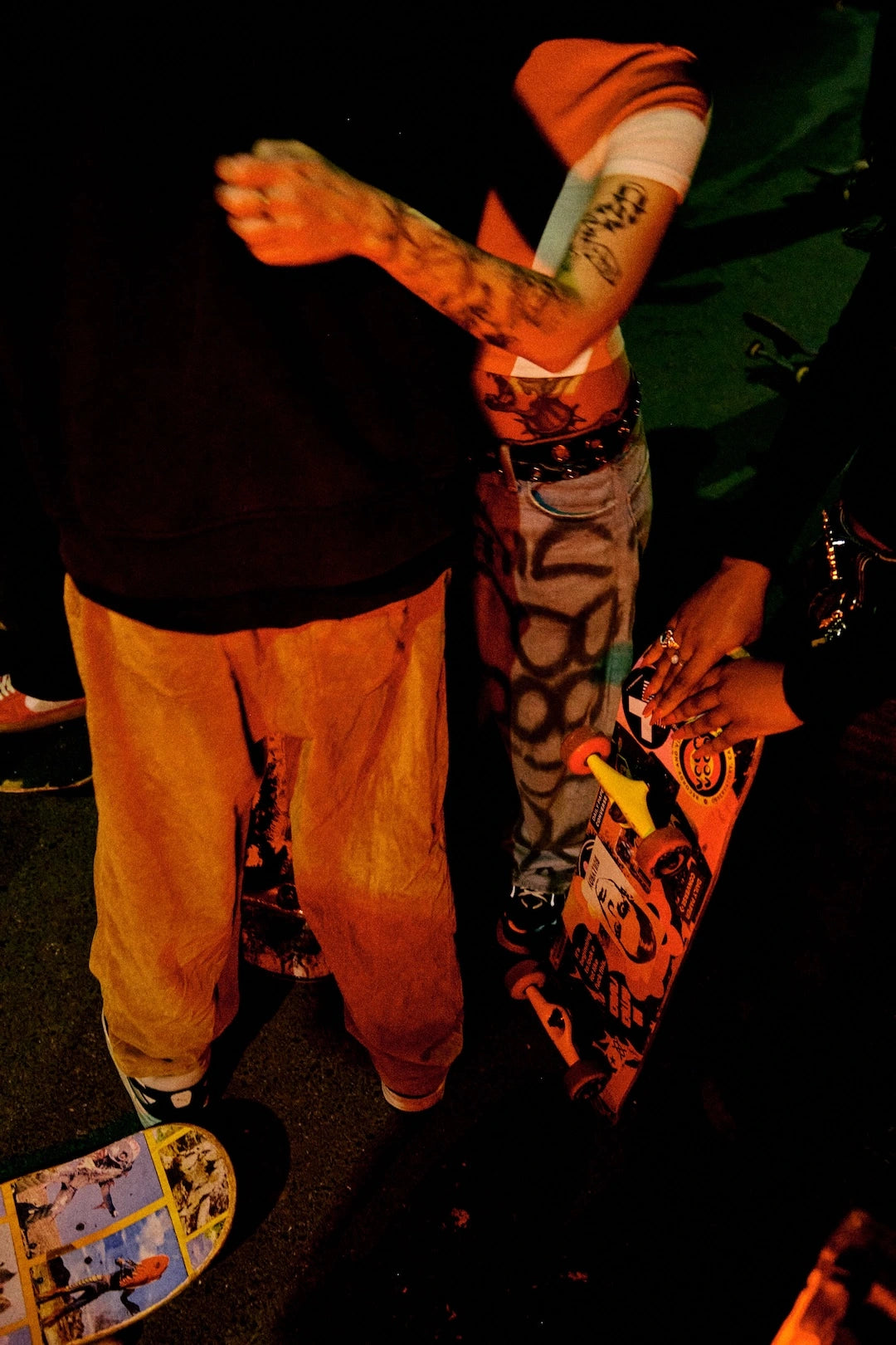 Person with tattoos holding a colorful skateboard in a dark setting