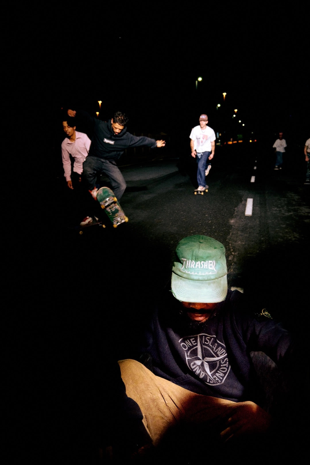 Skateboarders at night with one wearing a green cap and visible brand logo.