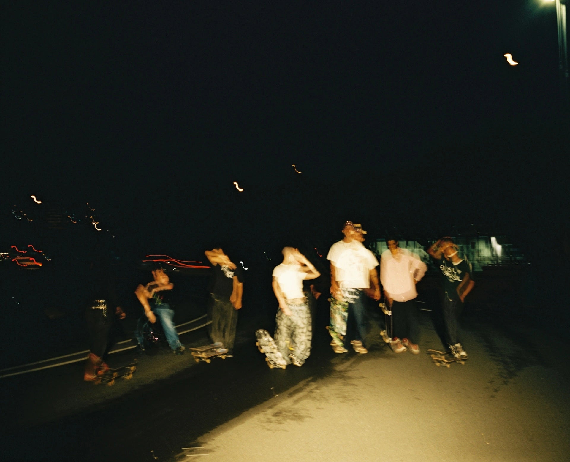 Group of people with skateboards at night on a dark street.