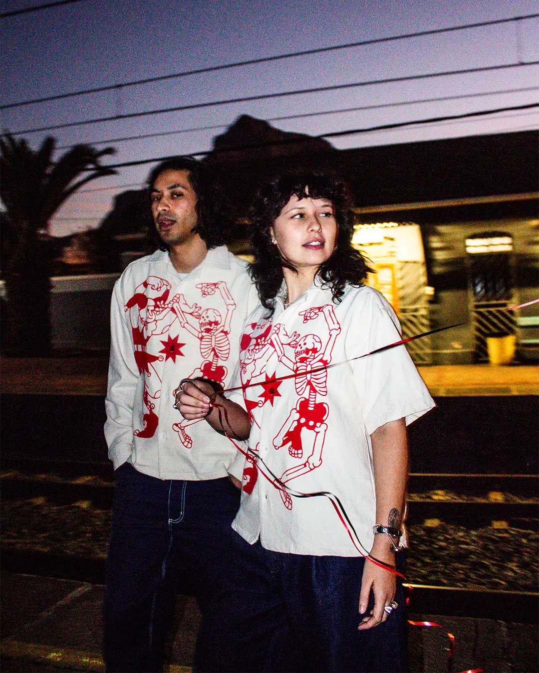 A trendy couple stands near the Cape Town train tracks at night while wearing the new BullyWopp button up shirts