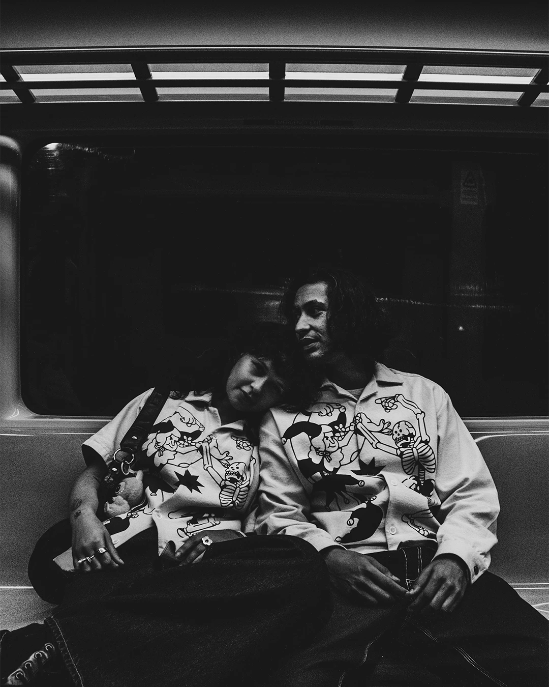 A couple sits in a train wearing the BushyWopp boxy shirts