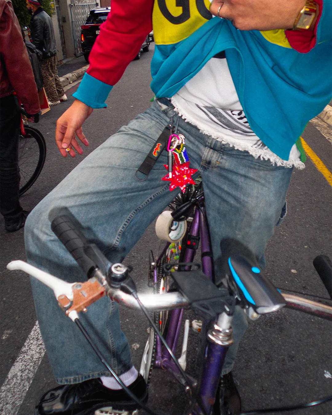 Male posing on a purple retro bicycle wearing trendy streetwear with the Bullyboy Star utility Keychain attached with a carabiner to his belt loop