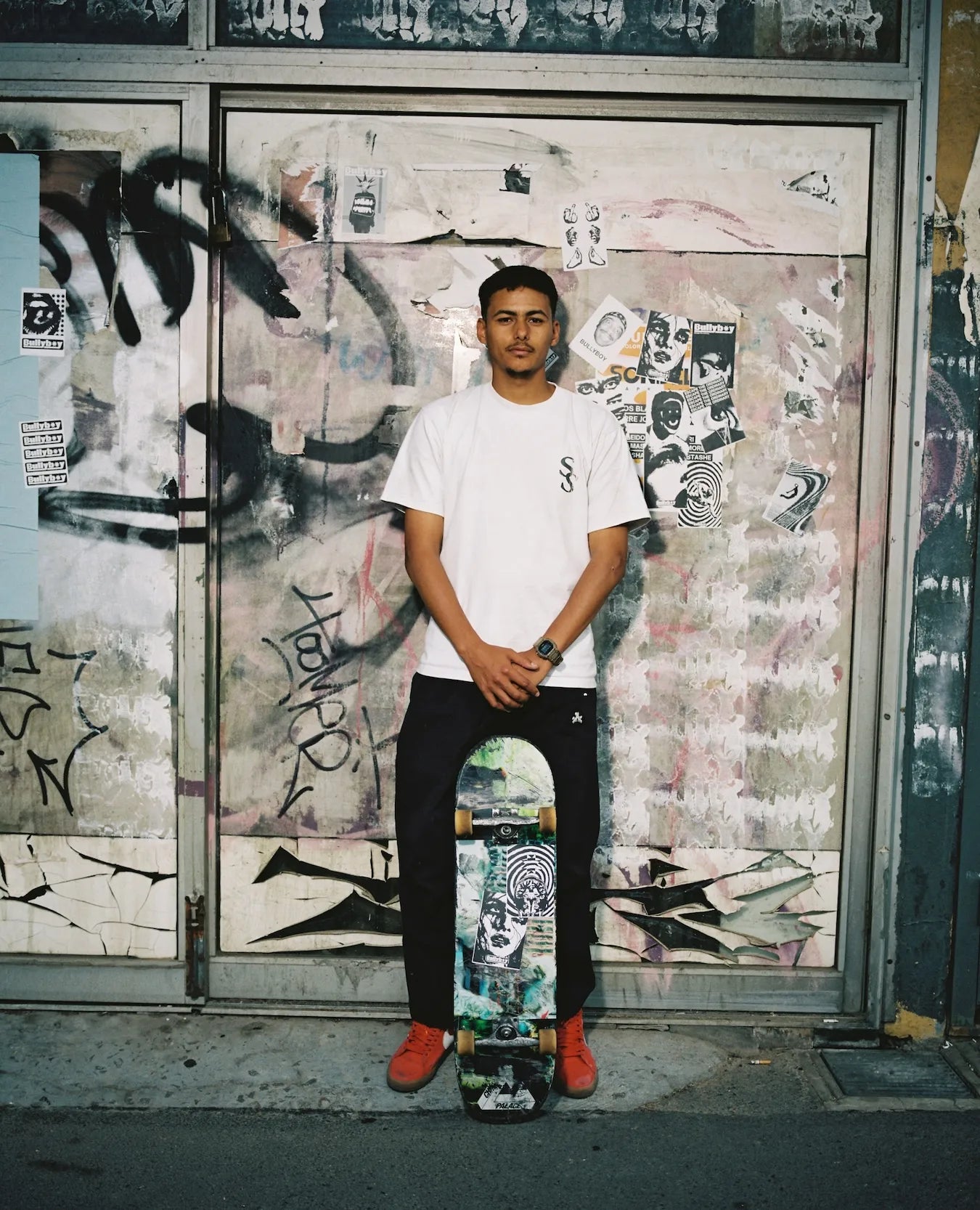 Person holding a skateboard in front of a graffiti-covered wall