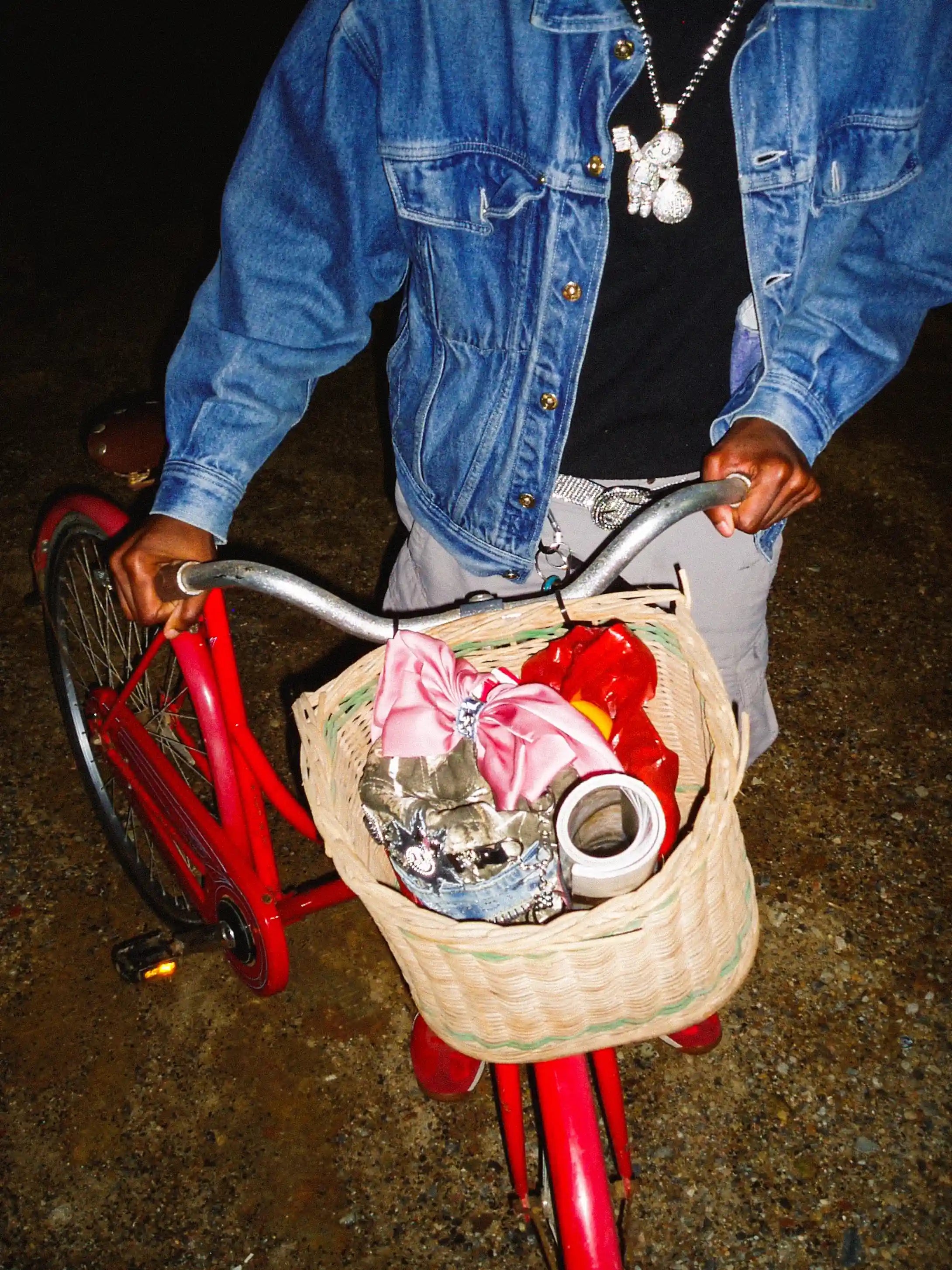 Person holding a red bicycle with a basket containing various items on a dark background