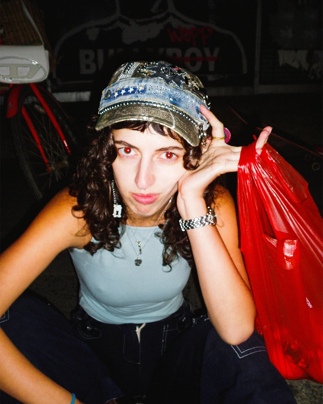 Person wearing a denim cap and blue top with a red plastic bag in a dark setting