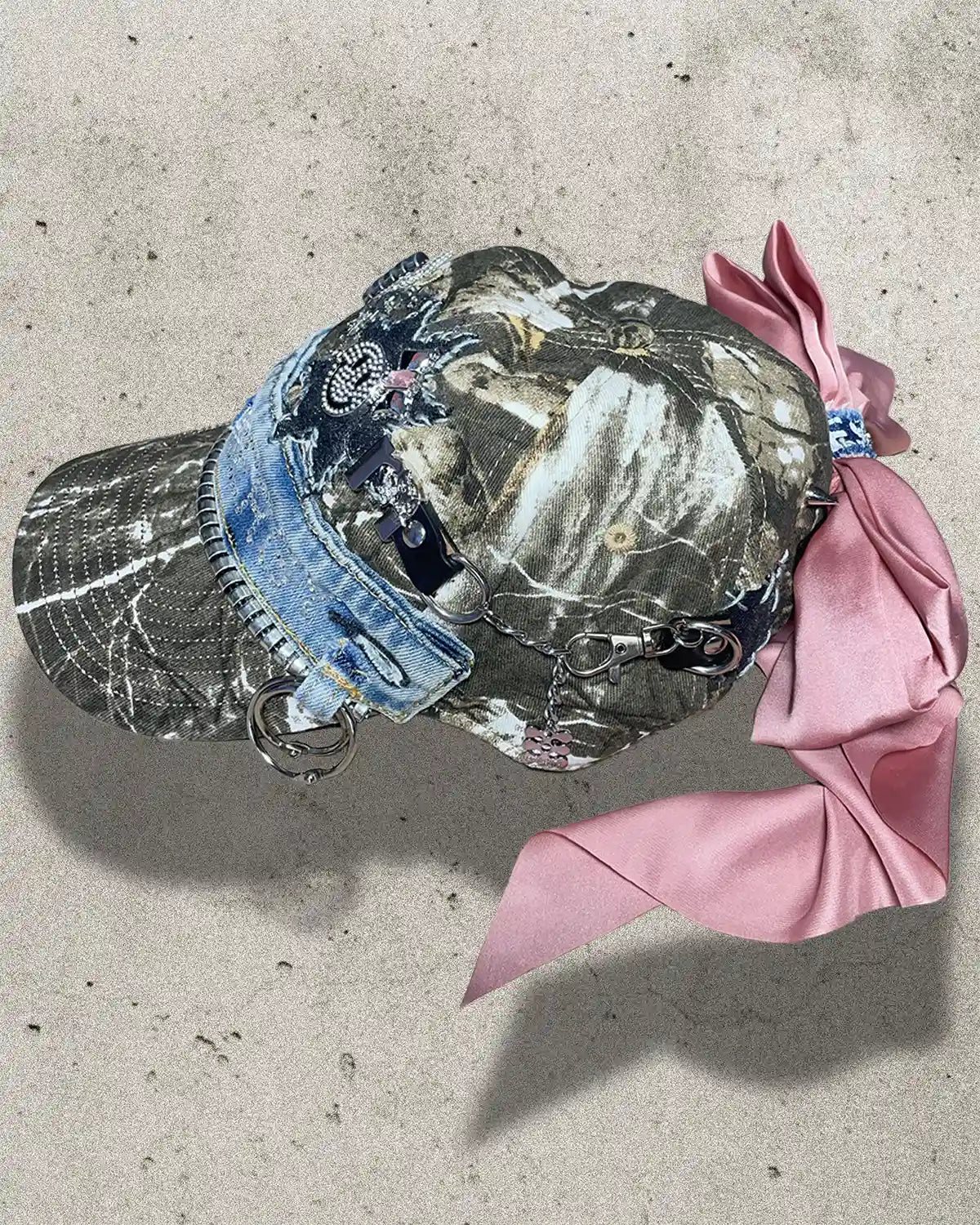Camouflage cap with denim brim and pink ribbon on a concrete surface
