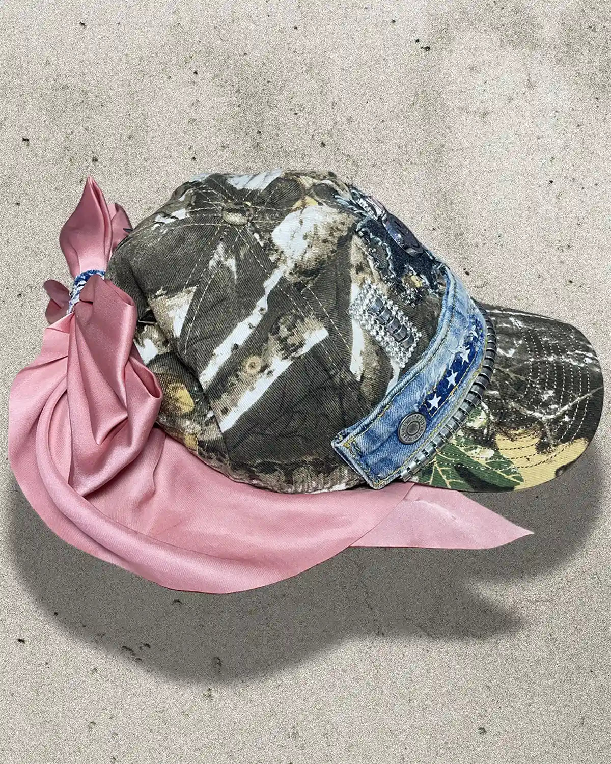 Camouflage cap with denim brim and pink scarf on a concrete surface