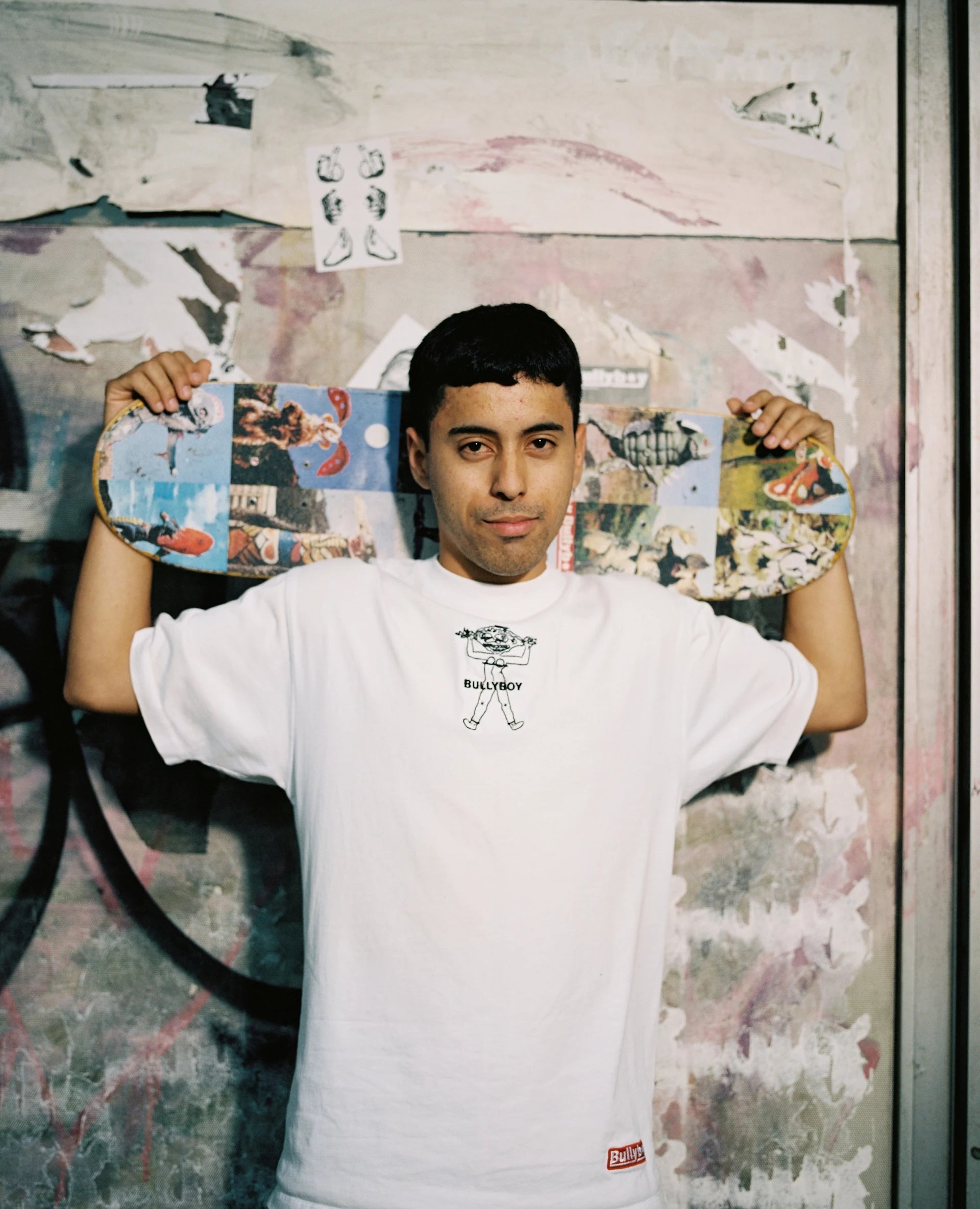 Person holding a colorful skateboard in front of a graffiti-covered wall