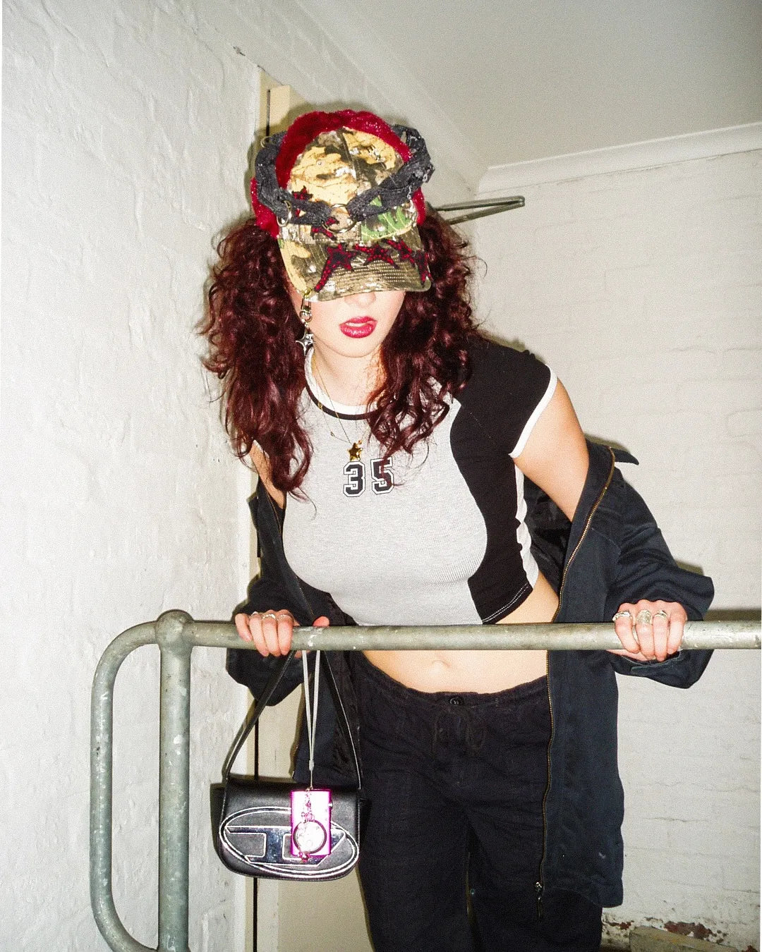 Person wearing a camouflage visor and black jacket with a white shirt, holding a handbag.