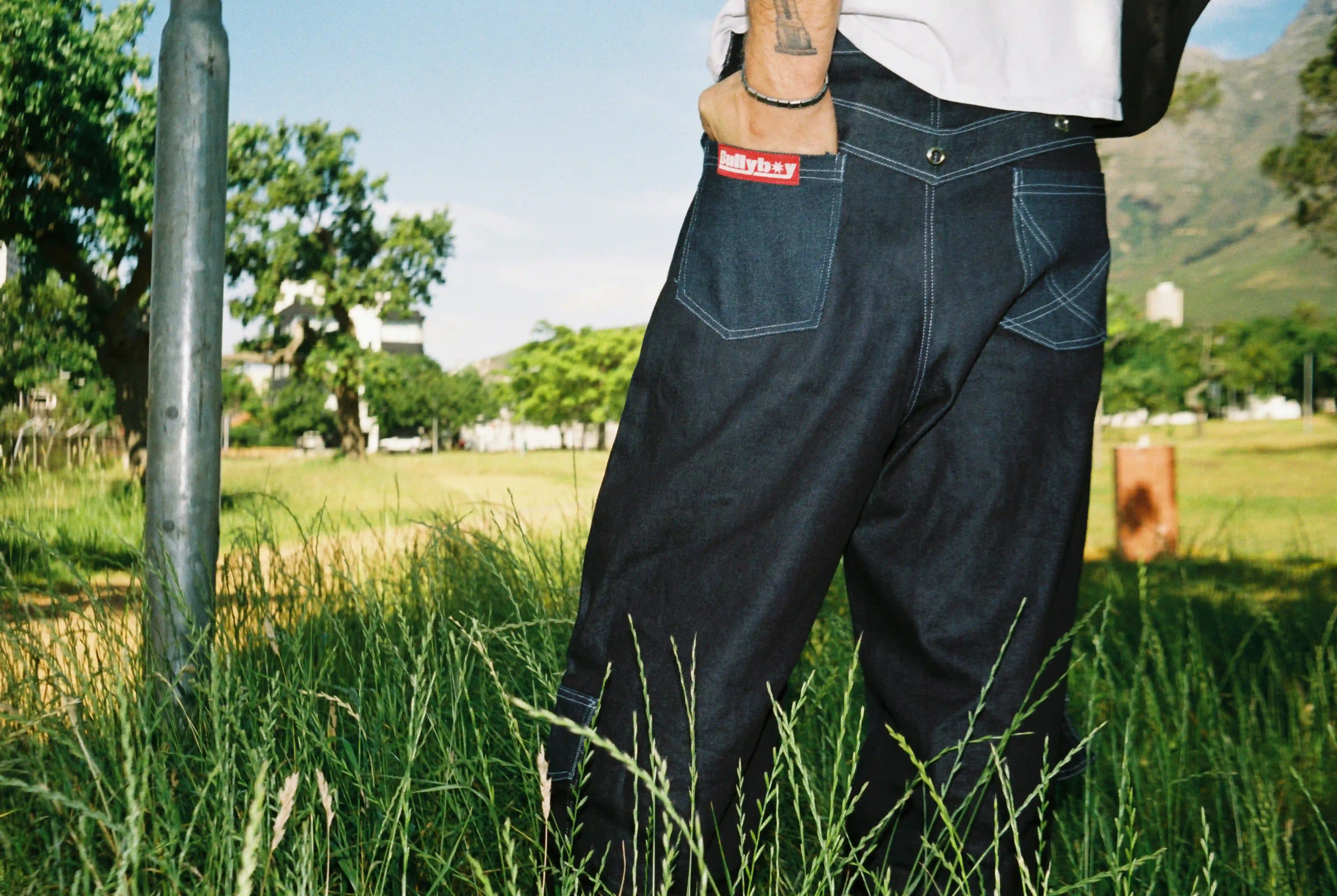 A man in premium Bullyboy streetwear stands in lush grass, gazing into the distance during a Cape Town photoshoot.