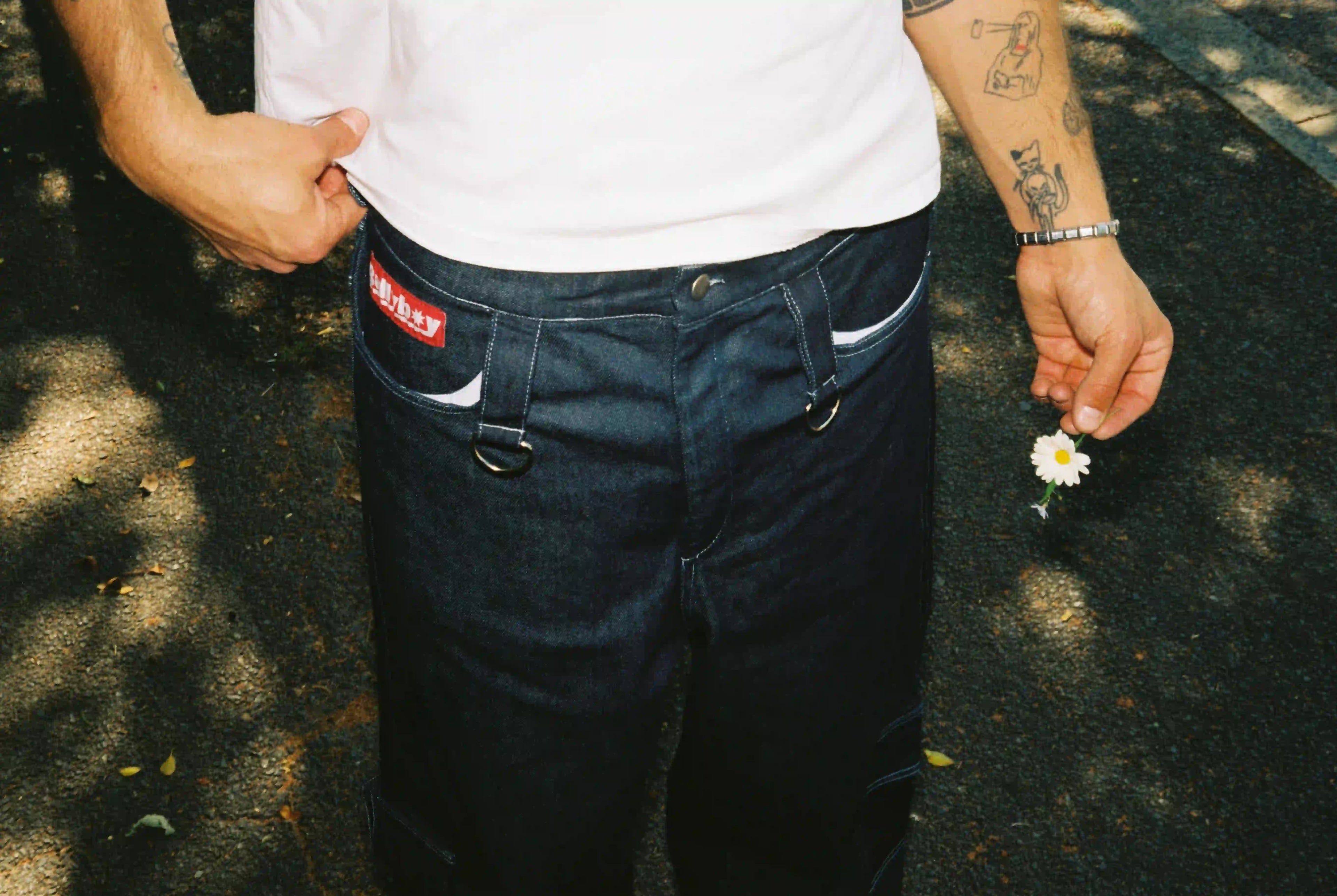 A stylish man with a tattoo on his arm gracefully holds a flower, embodying Bullyboy's premium streetwear in Cape Town.
