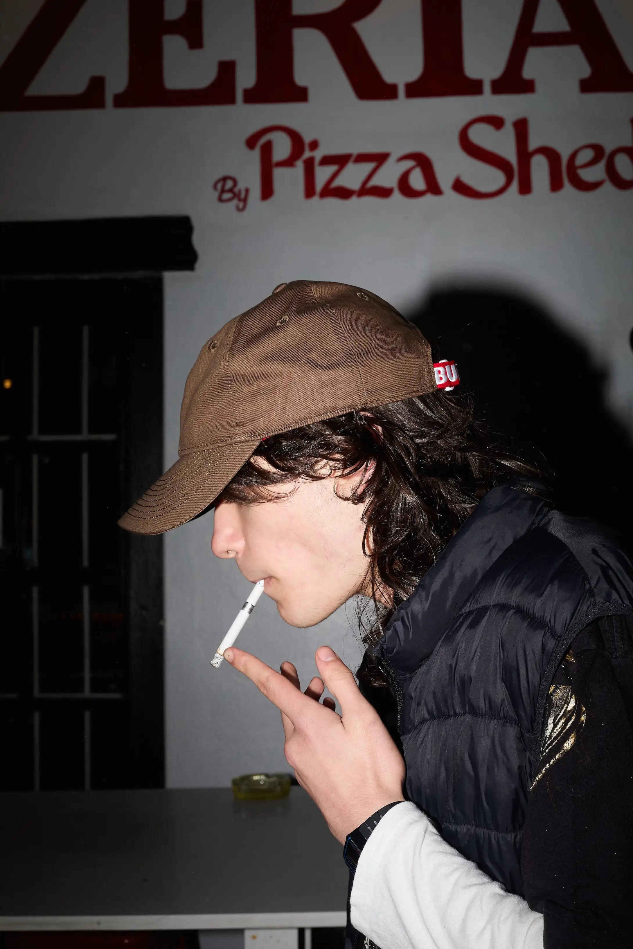Person smoking a cigarette in front of a Pizza Shed sign