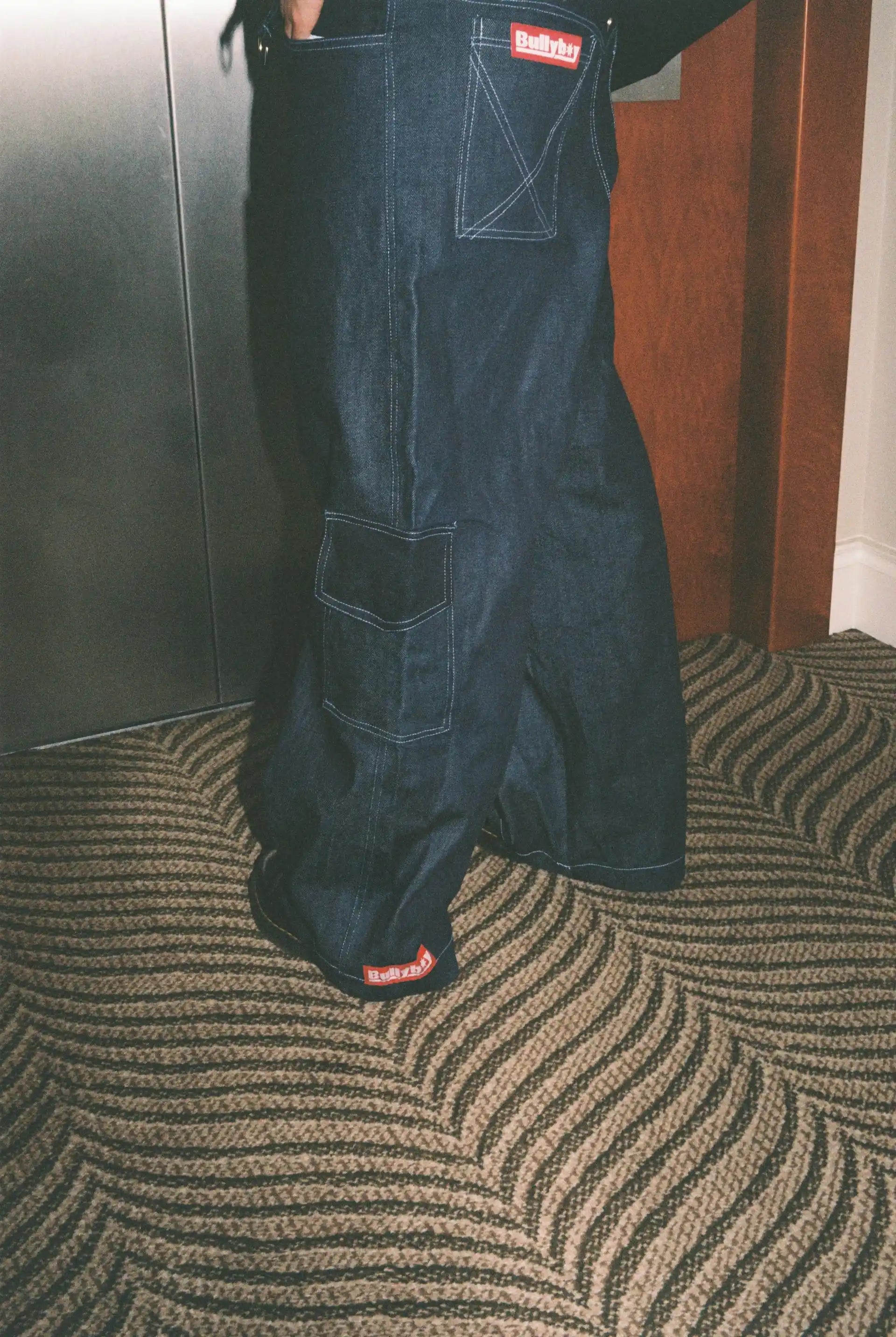 Dark blue denim overalls with a red label on a textured carpeted floor.
