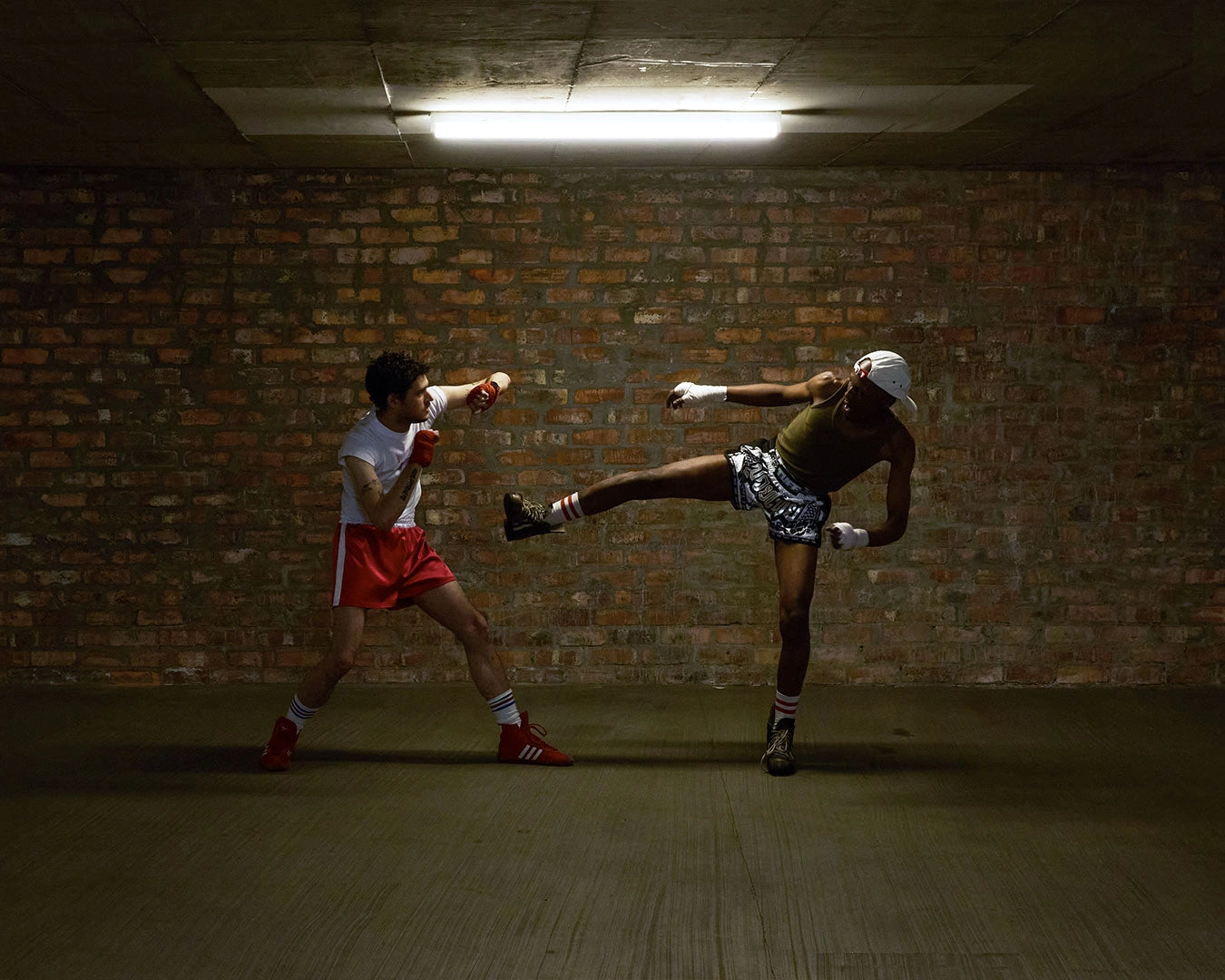 Two people practicing martial arts in a dimly lit room with brick walls.