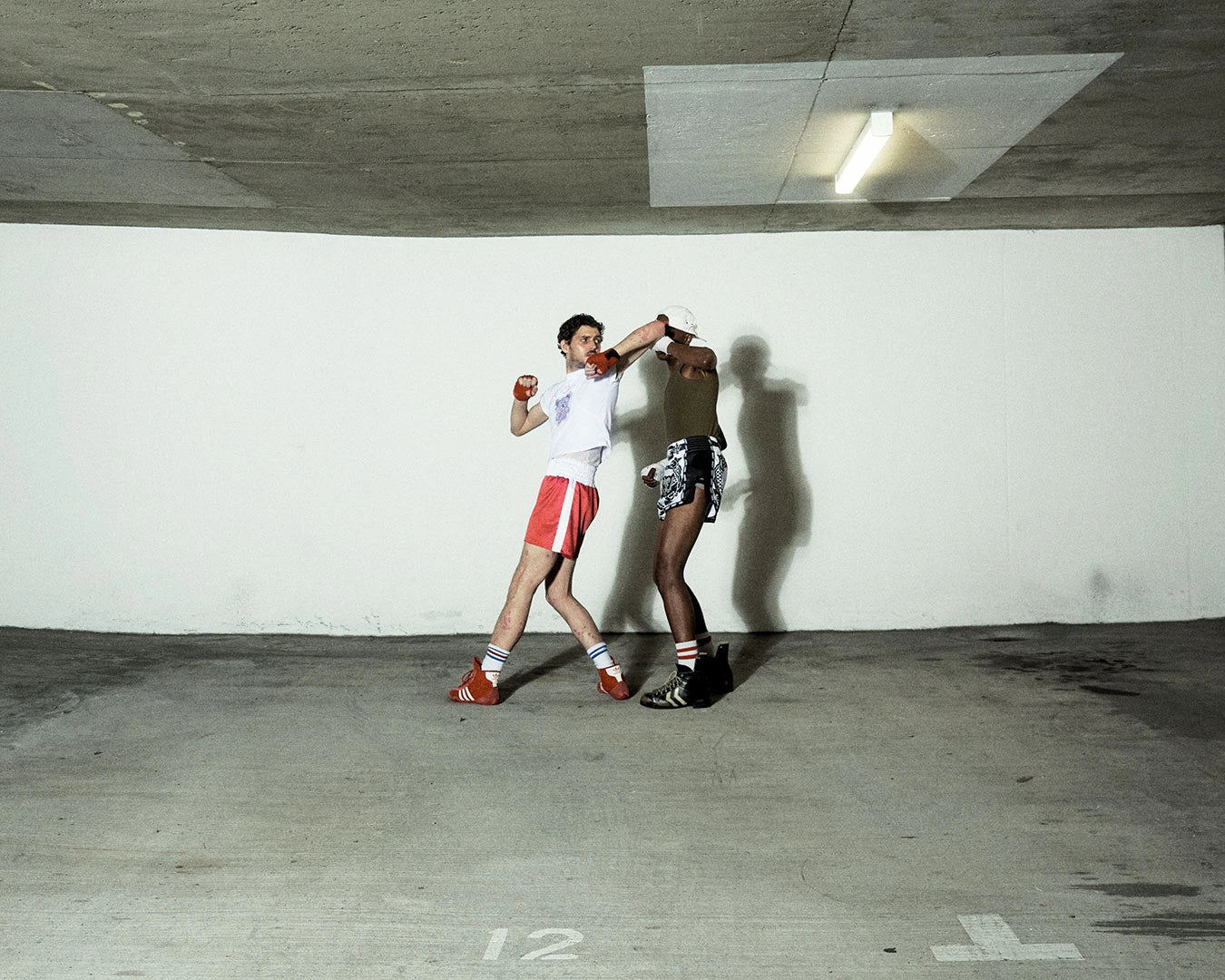 Two people in a boxing stance in an underground parking garage.