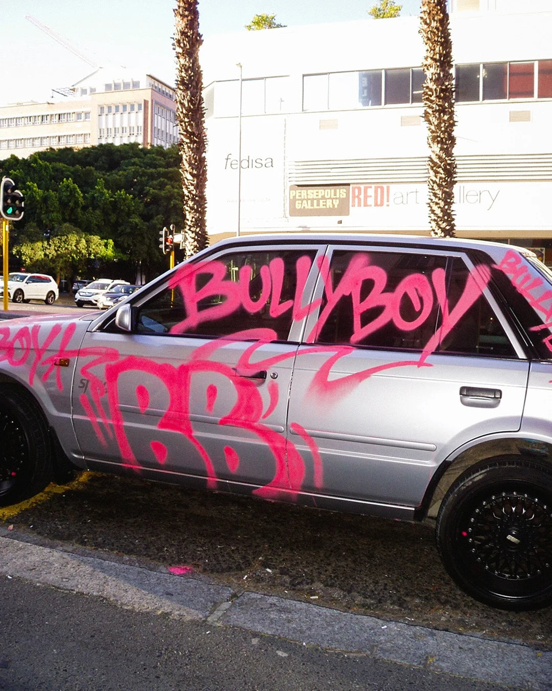 Silver car with pink graffiti on a city street