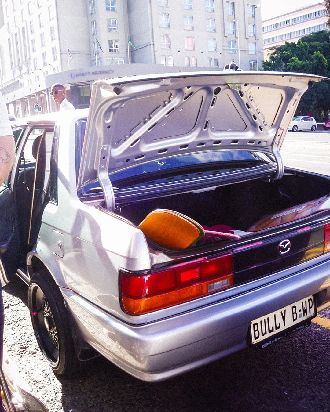 Back of a silver car with open trunk, showing a yellow kayak inside, on a street.