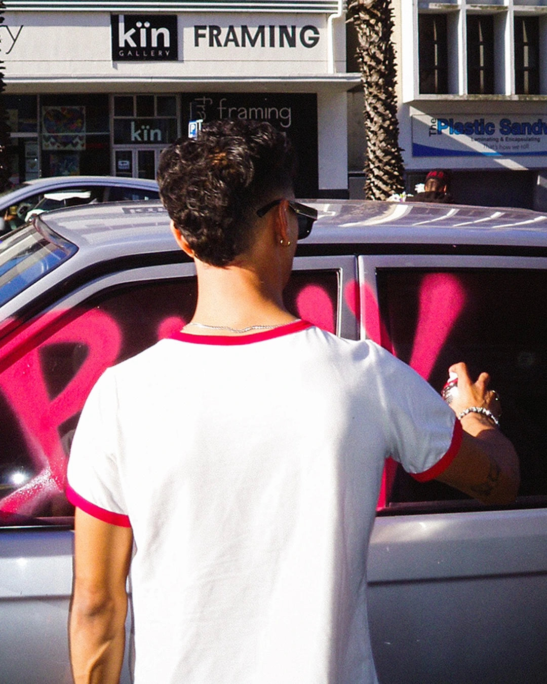Person standing next to a car with pink graphics, looking at a store front.