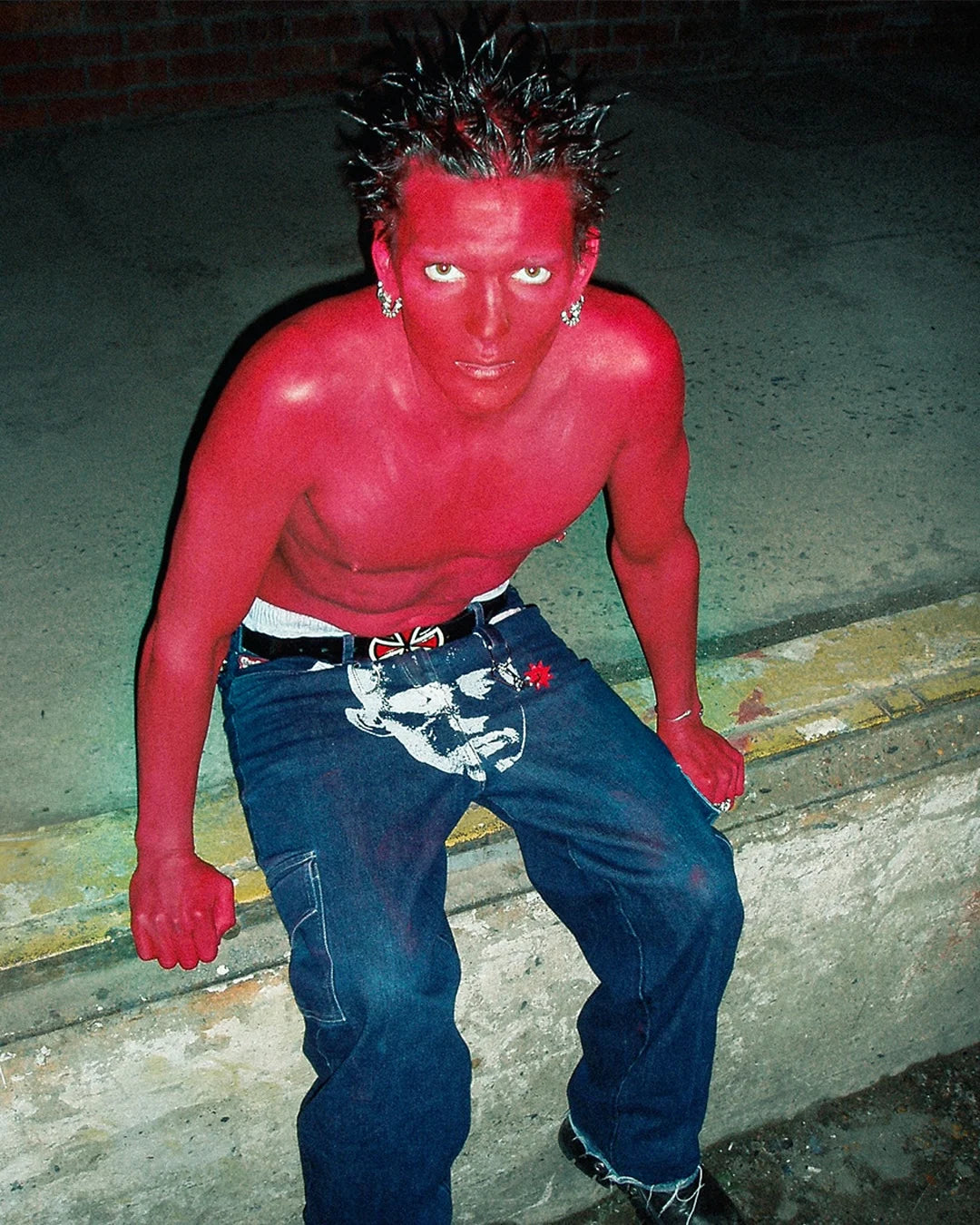 Person with red skin and spiky hair posing outdoors on a concrete surface.