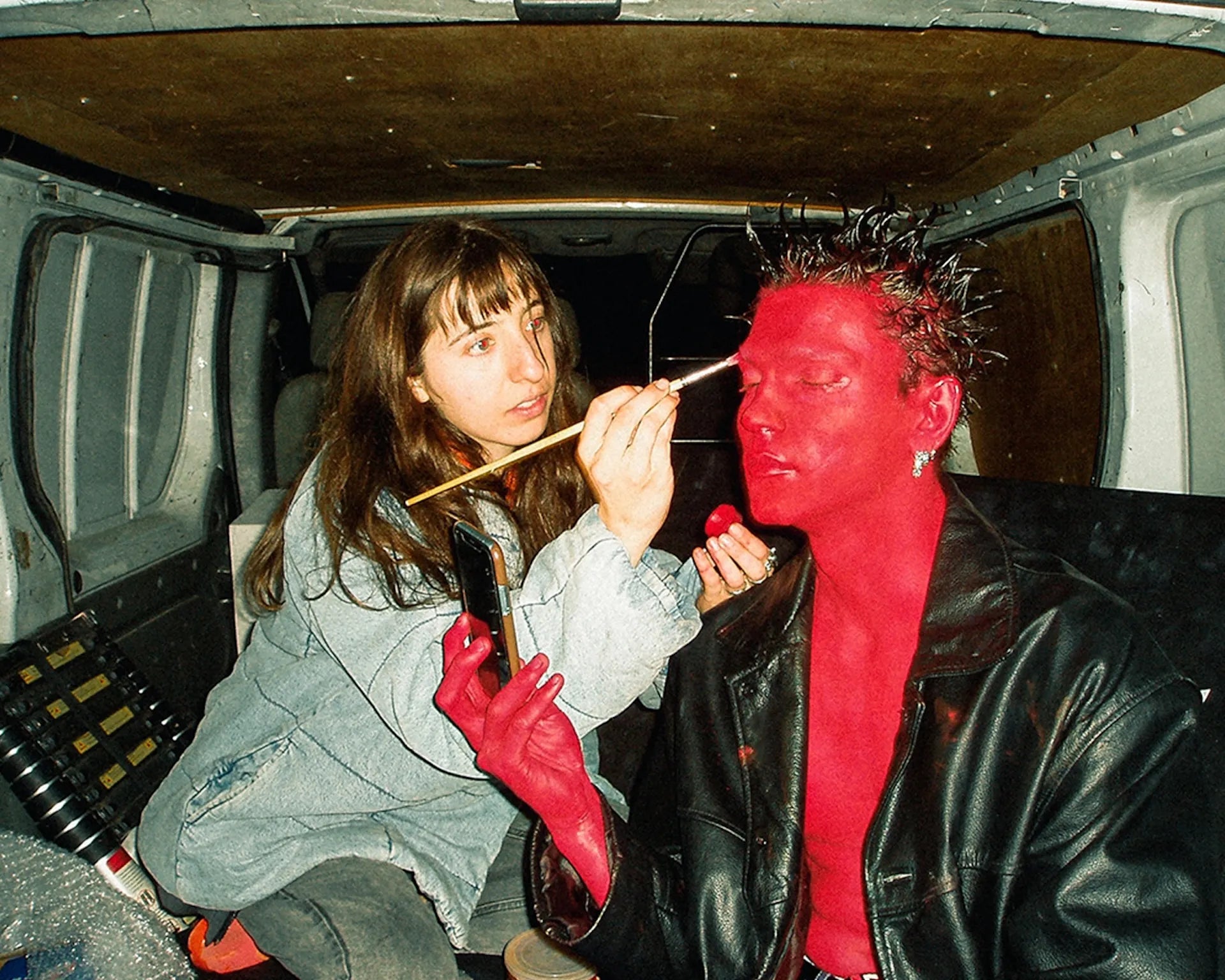 Person applying red paint to another person's face inside a vehicle.
