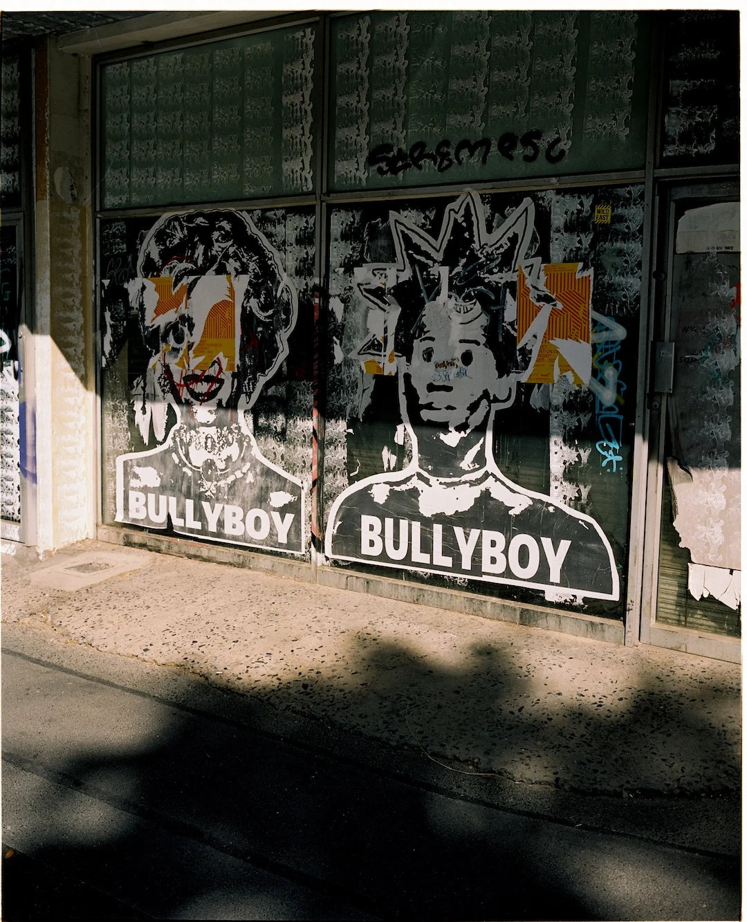 Stenciled images of 'Bullyboy' on a glass door with graffiti.