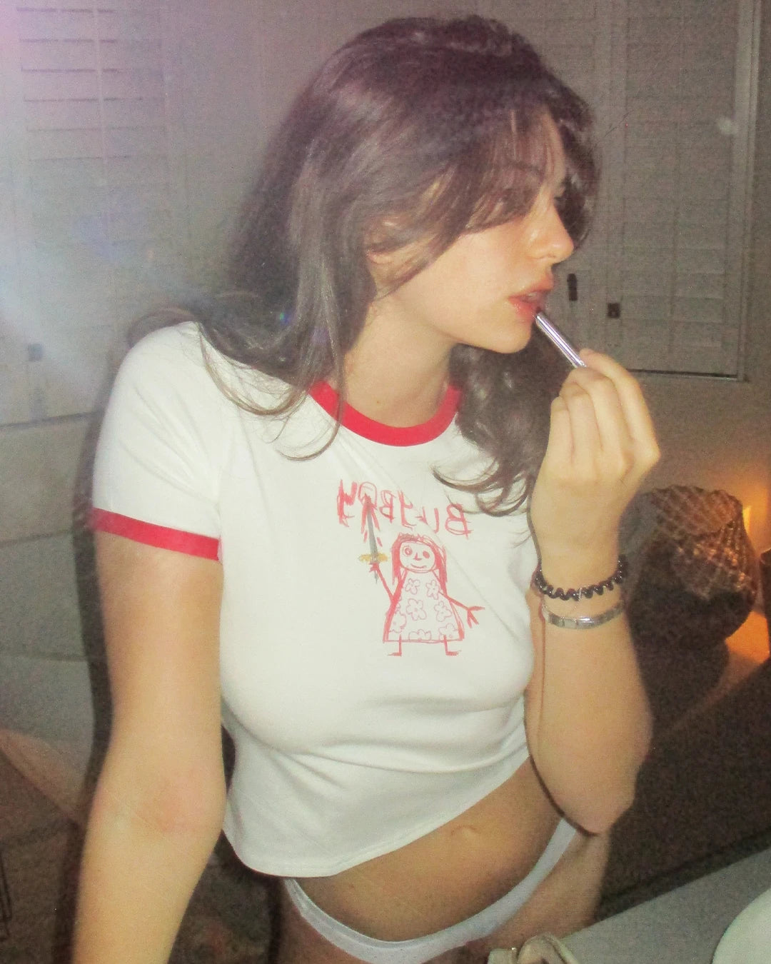 Attractive female model applies lipstick in bathroom candid shoot while wearing the new Bullyboy red ringer tee