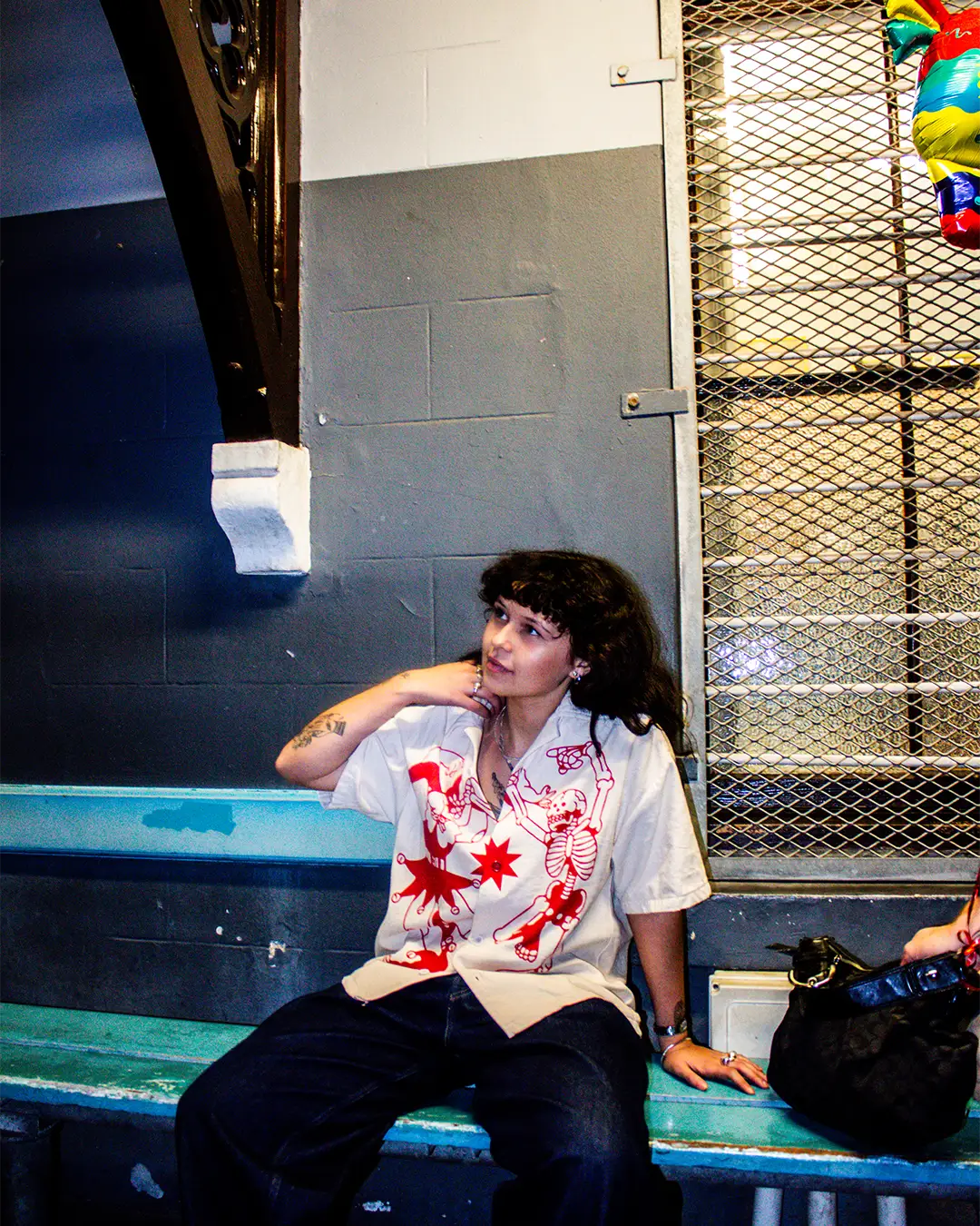 An alternative woman sits on a bench near the Cape Town train station at night while wearing the new BullyWopp button up shirts