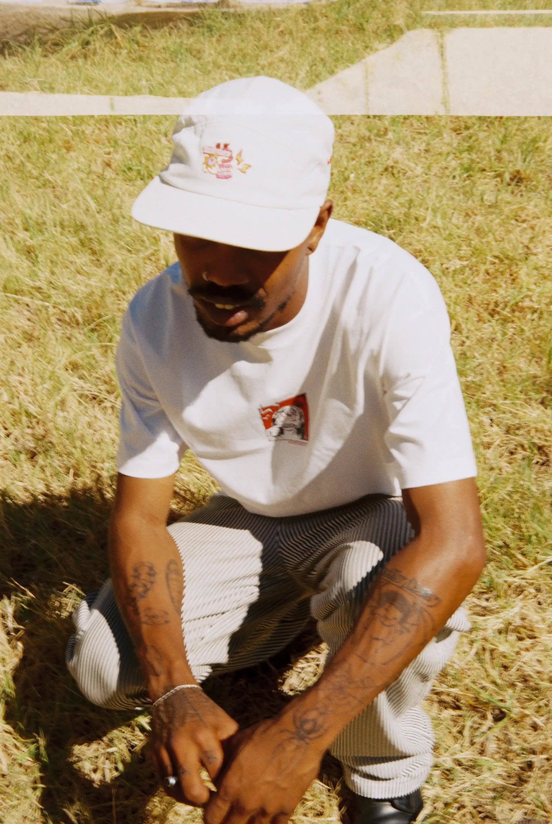 A man kneels in a field, showcasing Bullyboy premium streetwear, embodying South African fashion and a unique style