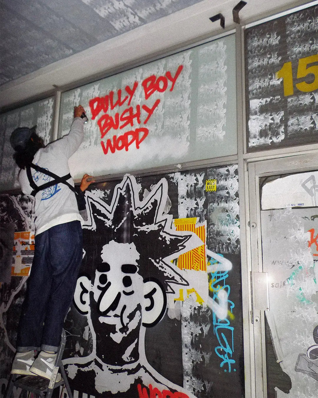Bushy Wopp spray paints Bullyboy and Bushy Wopp on a wall on Bree Street Cape Town with red paint