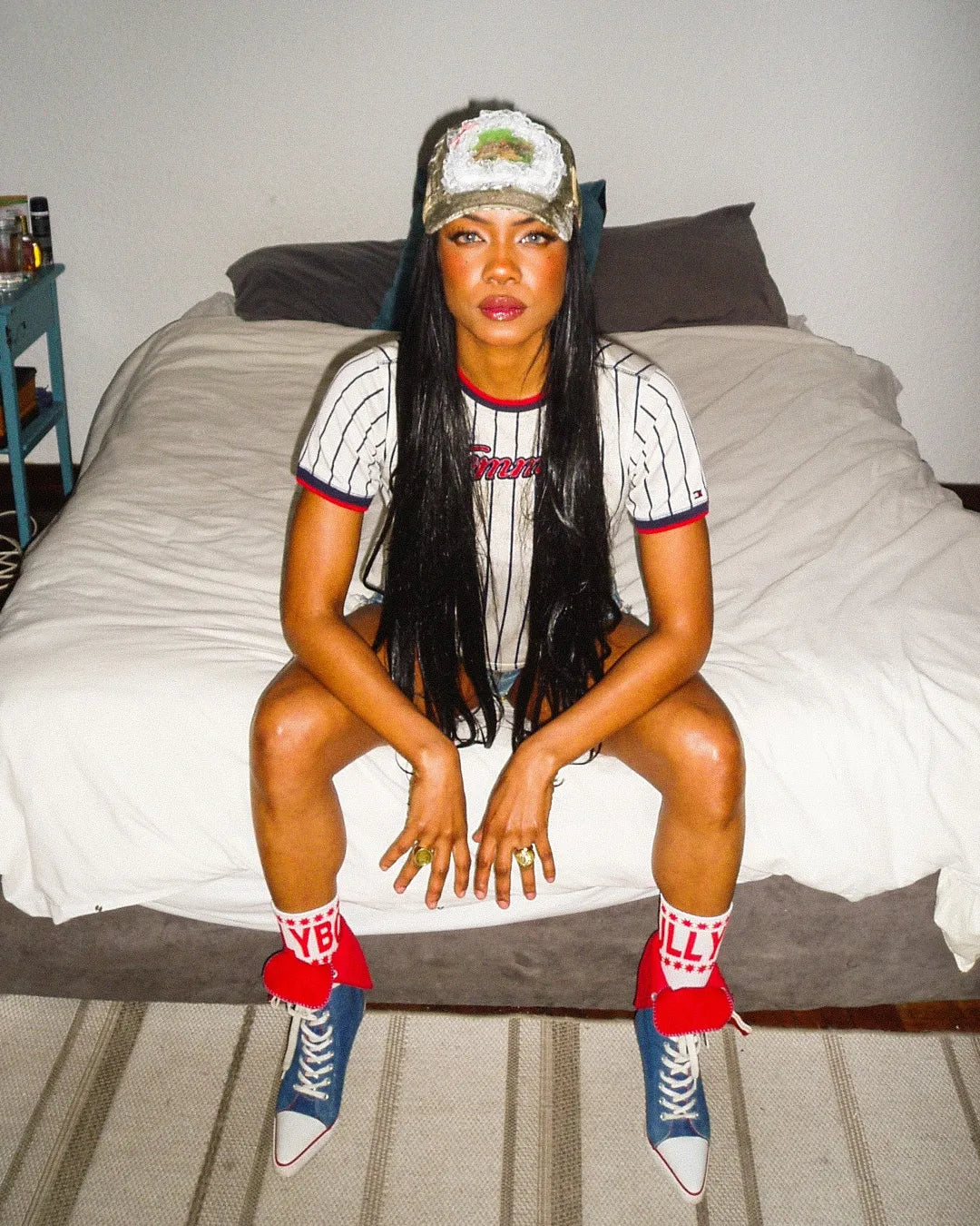 Person sitting on a bed wearing a sports jersey, cap, and colorful socks.