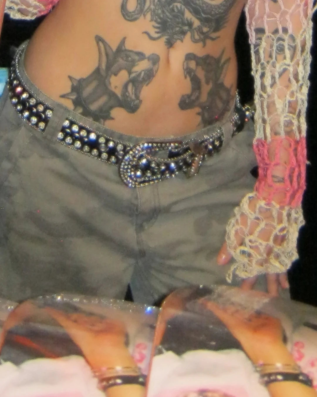 Close-up of a person's midriff with detailed tattoos of two wolves howling. The person embodies an edgy South African streetwear vibe with a studded belt and a pink mesh sleeve, exuding confidence like a true bullyboy.