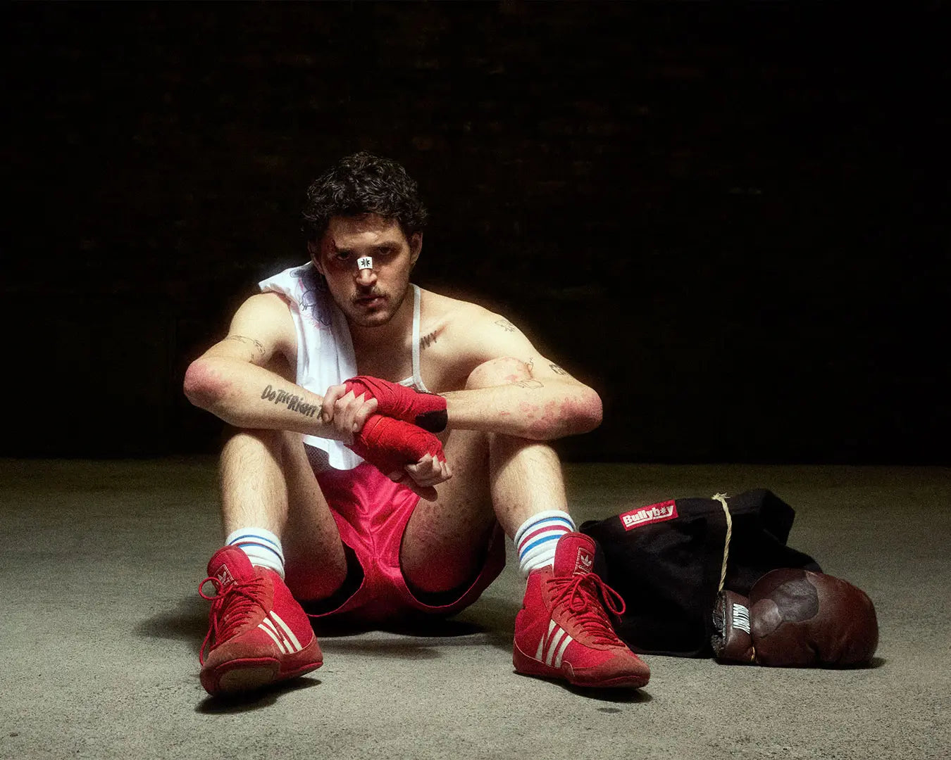 A stylish man in boxing gloves sits on the ground, representing Bullyboy's premium streetwear against a Cape Town backdrop.