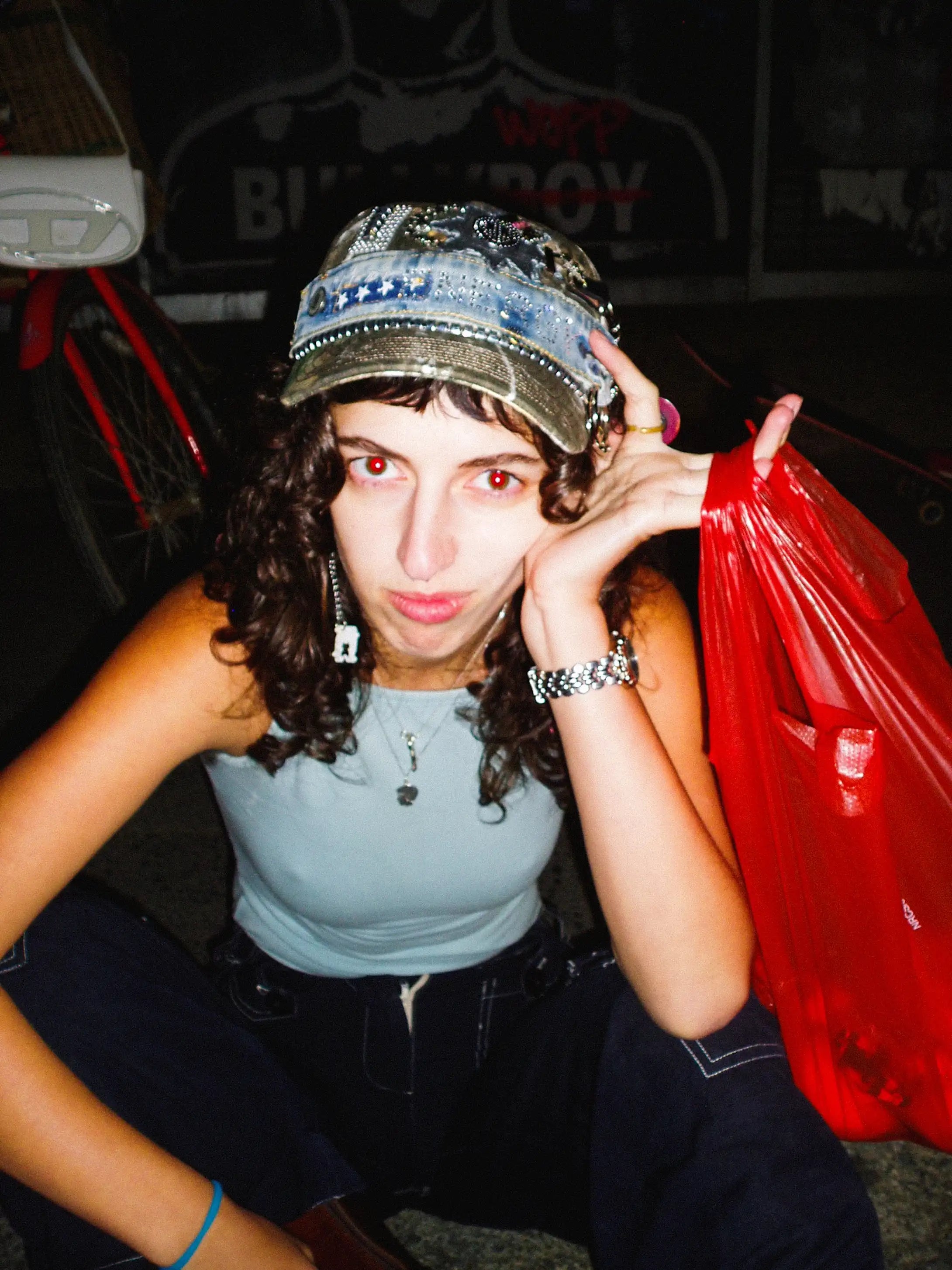 Person wearing a decorative cap with a red plastic bag in a dark setting