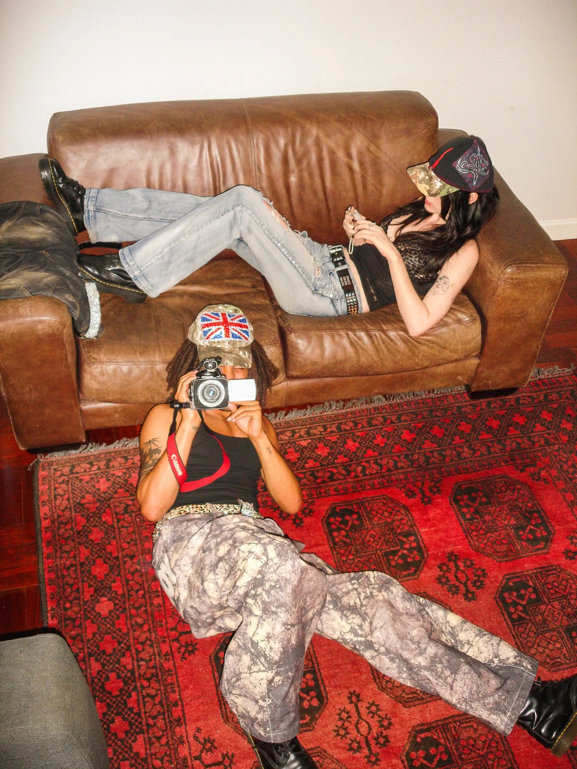 Two people on a brown leather couch with a red patterned rug underneath.