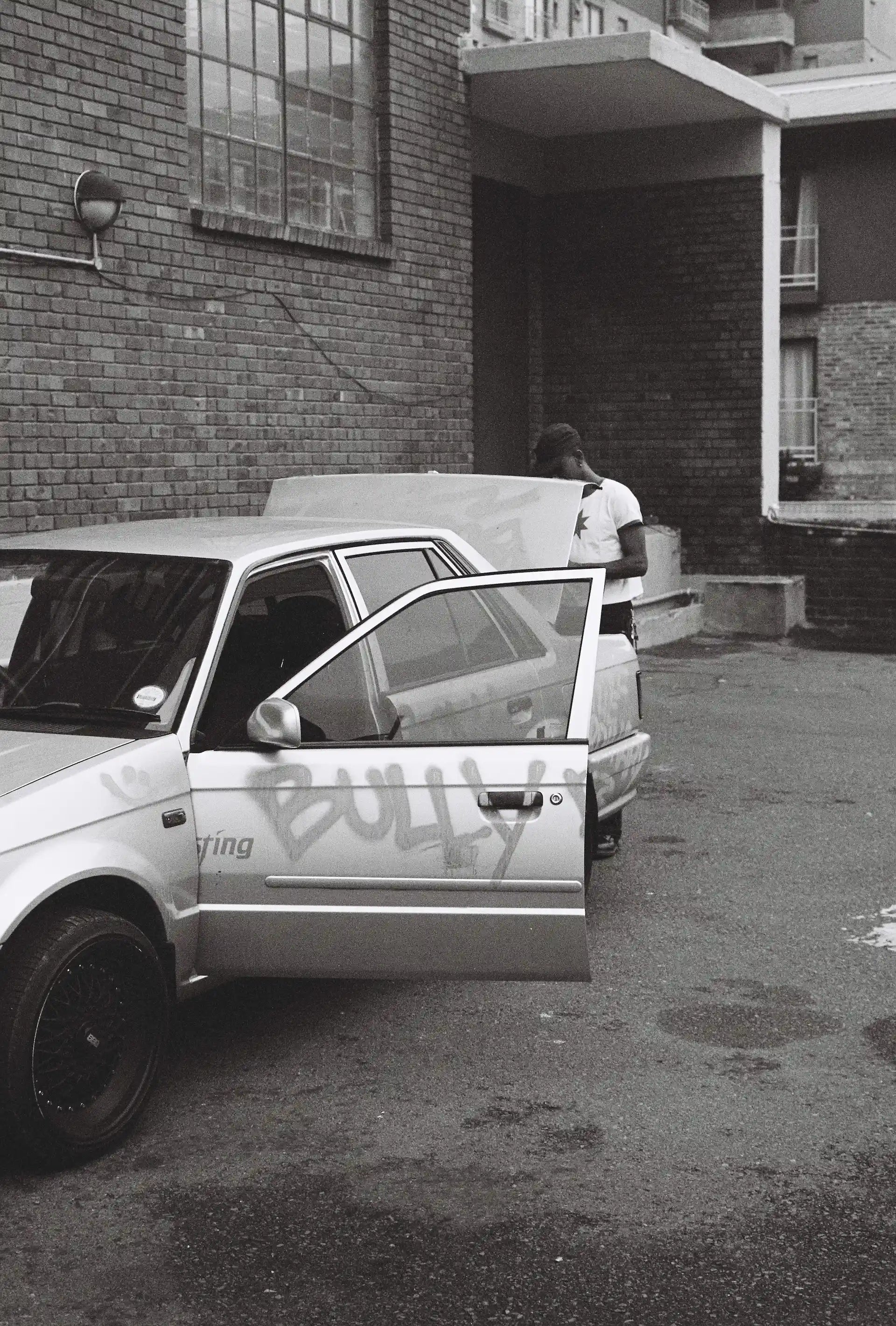Car with 'BULLY' spray-painted on the side, parked in an urban setting.
