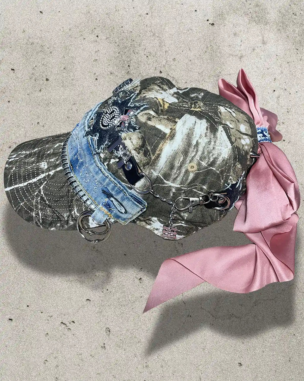 Camouflage cap with denim brim and pink ribbon on a concrete surface
