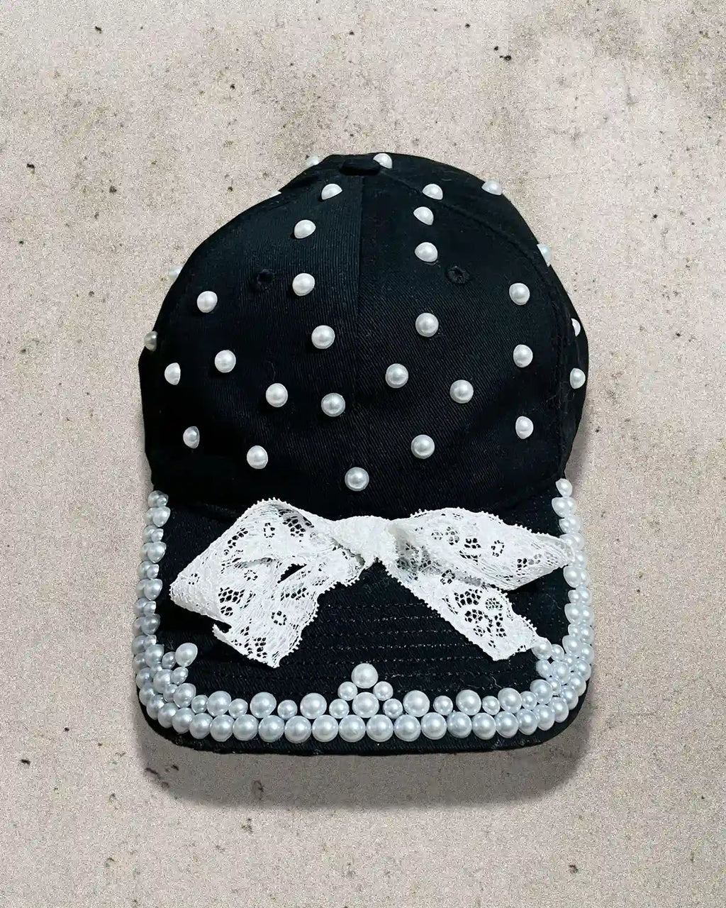 Black cap decorated with white pearls, lace trimming, and a delicate bow.