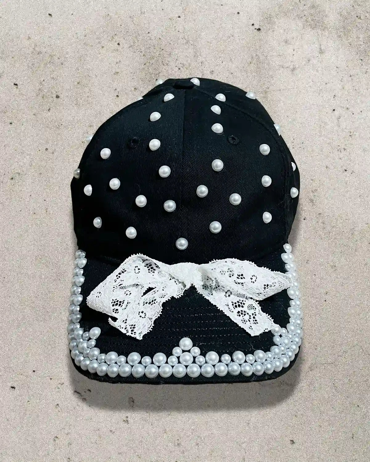 Black cap decorated with white pearls, lace trimming, and a delicate bow.