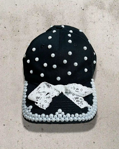 Black cap decorated with white pearls, lace trimming, and a delicate bow.